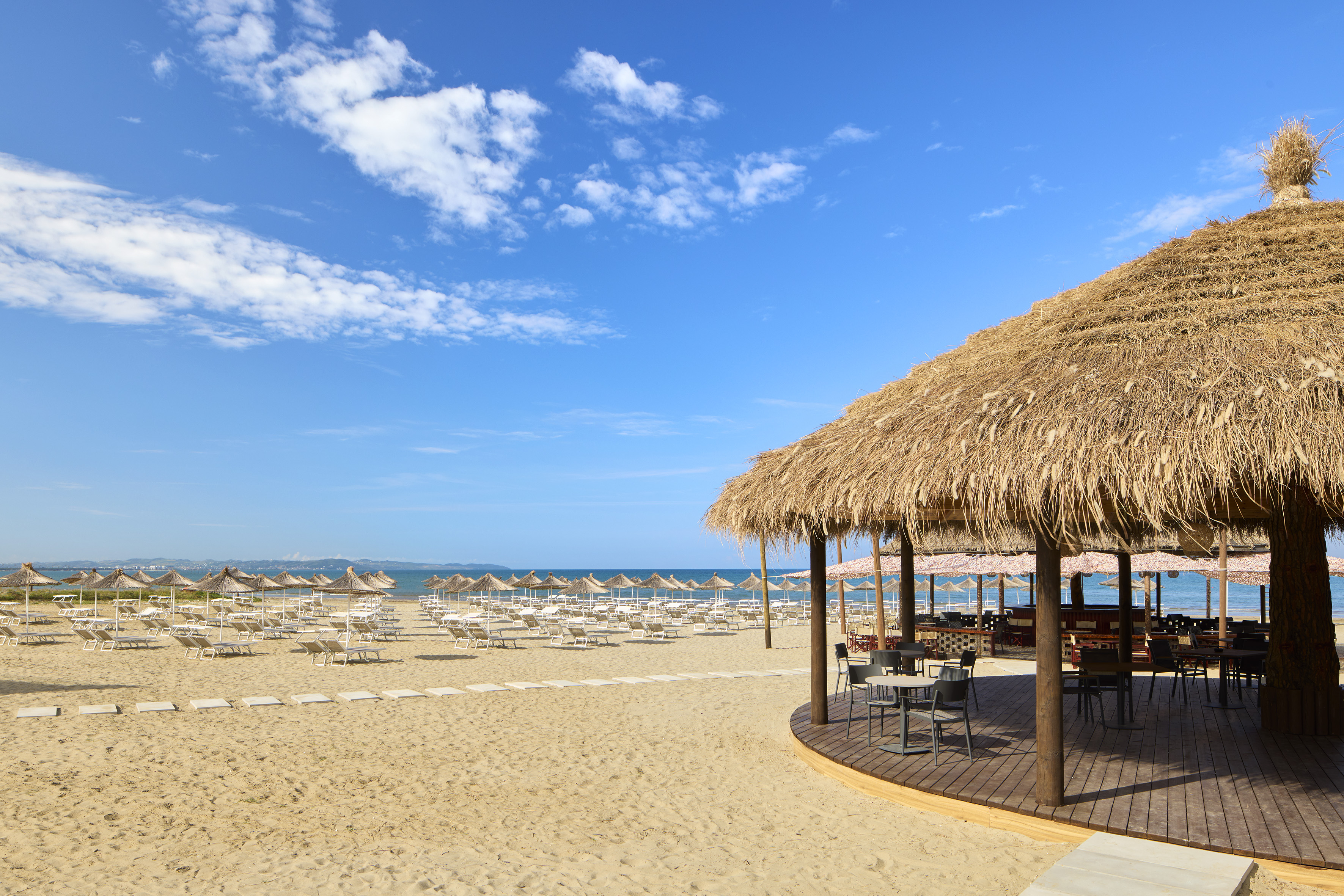 a beach with a thatched roof and chairs