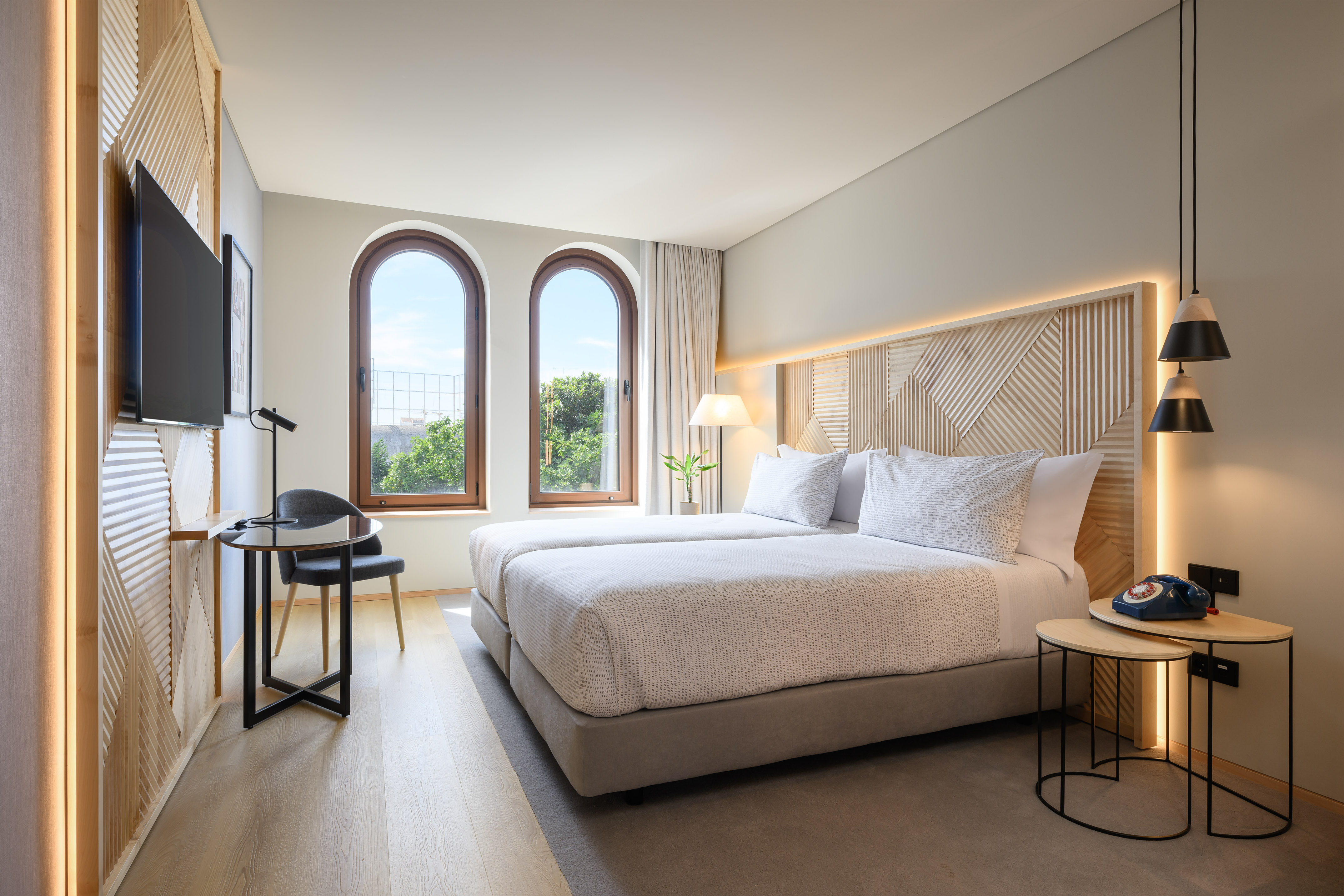 Contemporary hotel bedroom with twin beds, arched windows, and wood paneling.