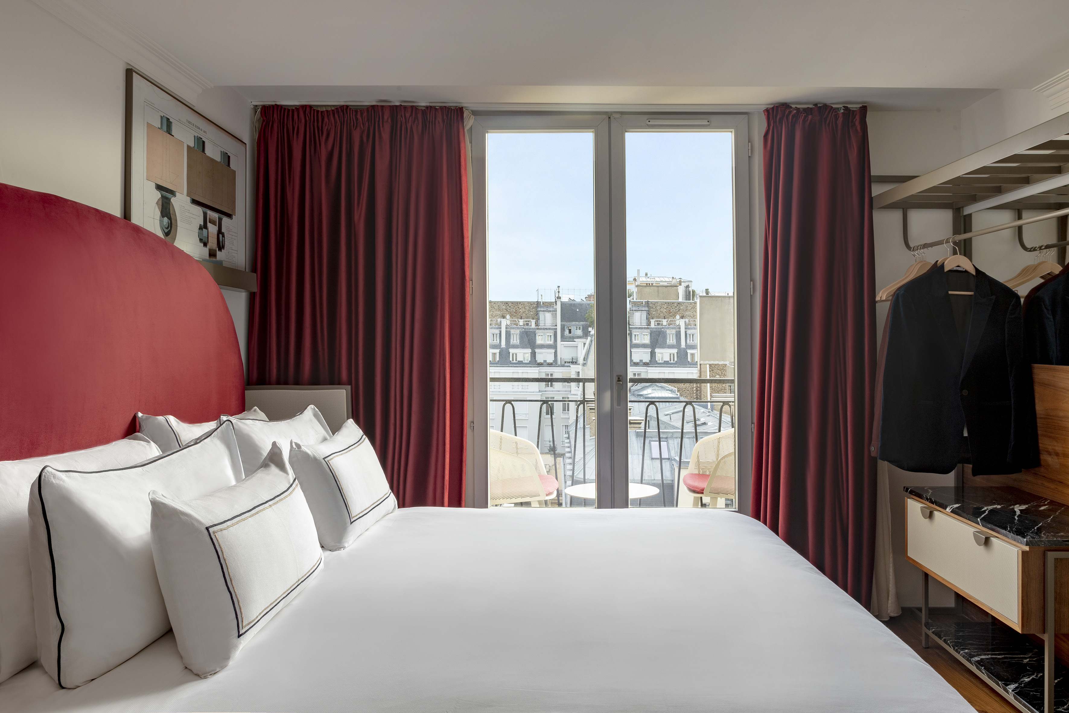 Stylish hotel room with red headboard, white bed, balcony, and Paris city view.