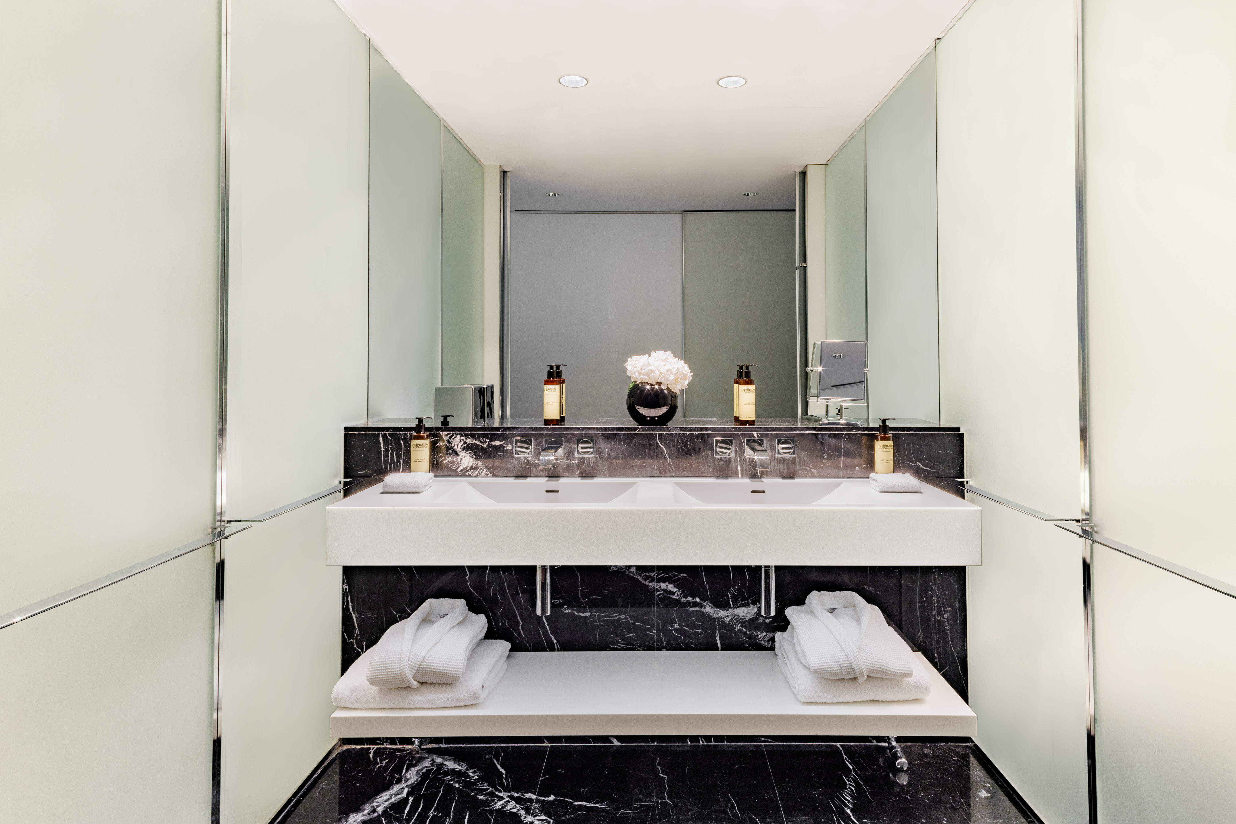 Modern luxury double vanity bathroom with black marble, white sinks, bathrobes.