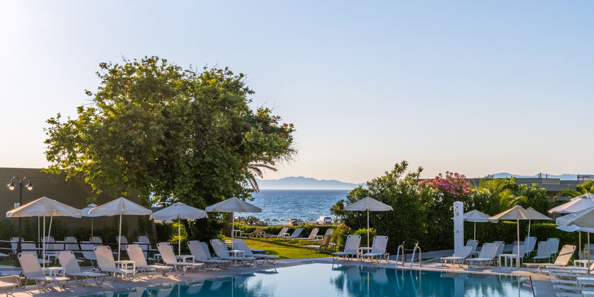 Resort swimming pool with sun loungers, ocean view, and clear blue sky.