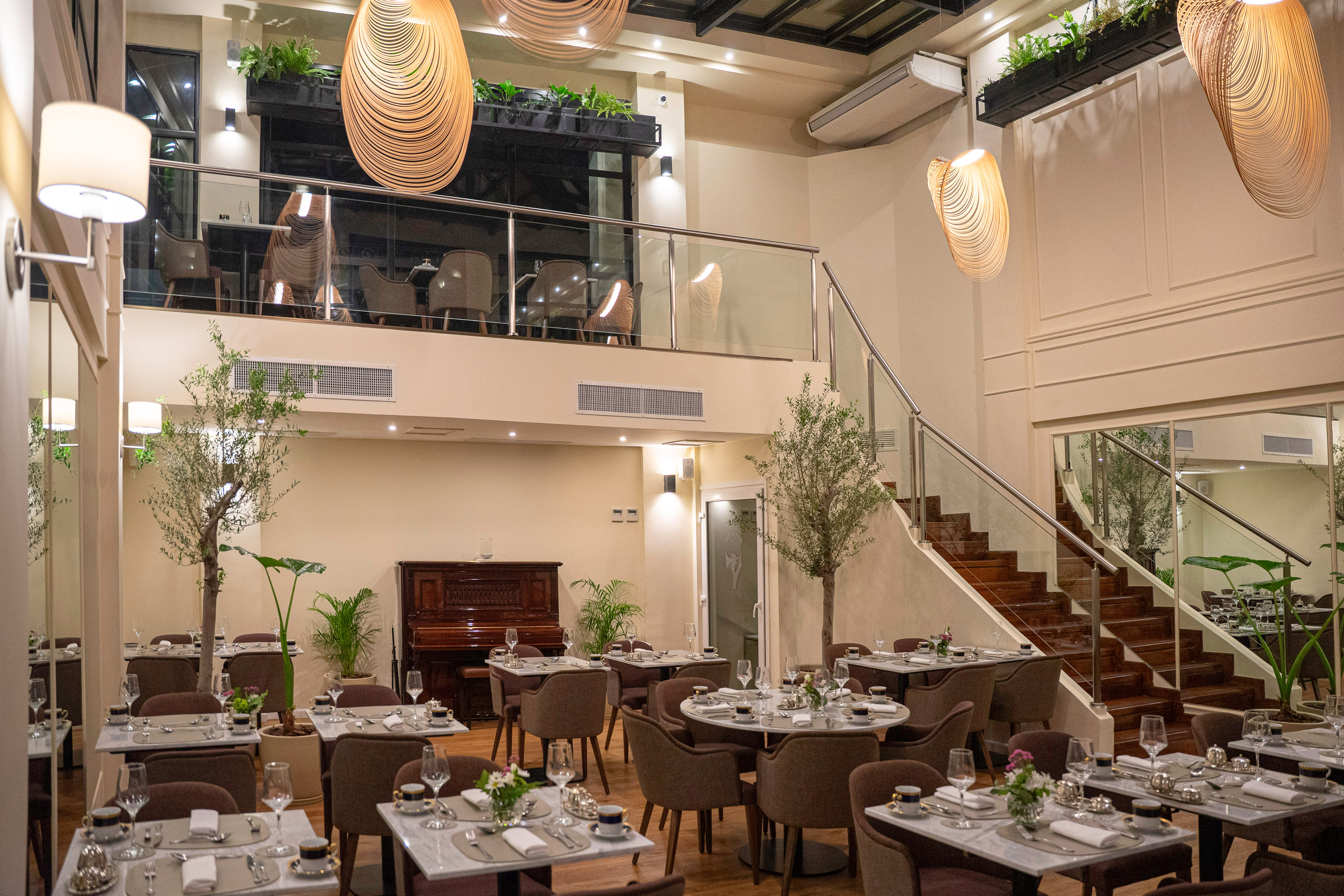 Elegant two-story restaurant interior with dining tables, mezzanine, piano, and plants.