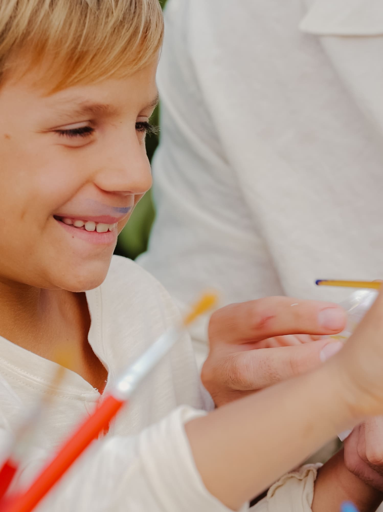 Boy with paint on lip smiles while painting with an adult.