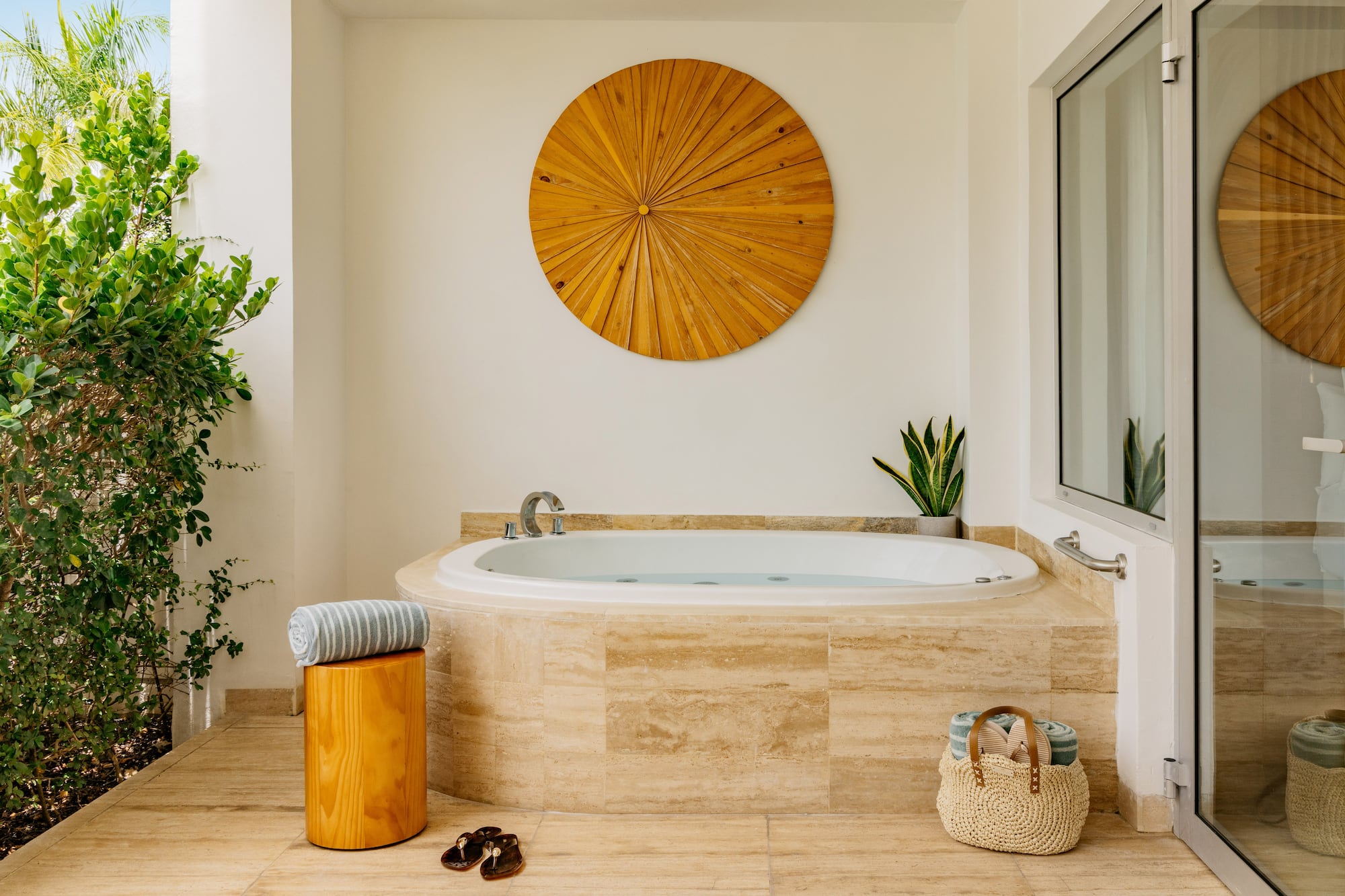 Luxury outdoor jacuzzi on patio with wood wall art, plants, and towels.