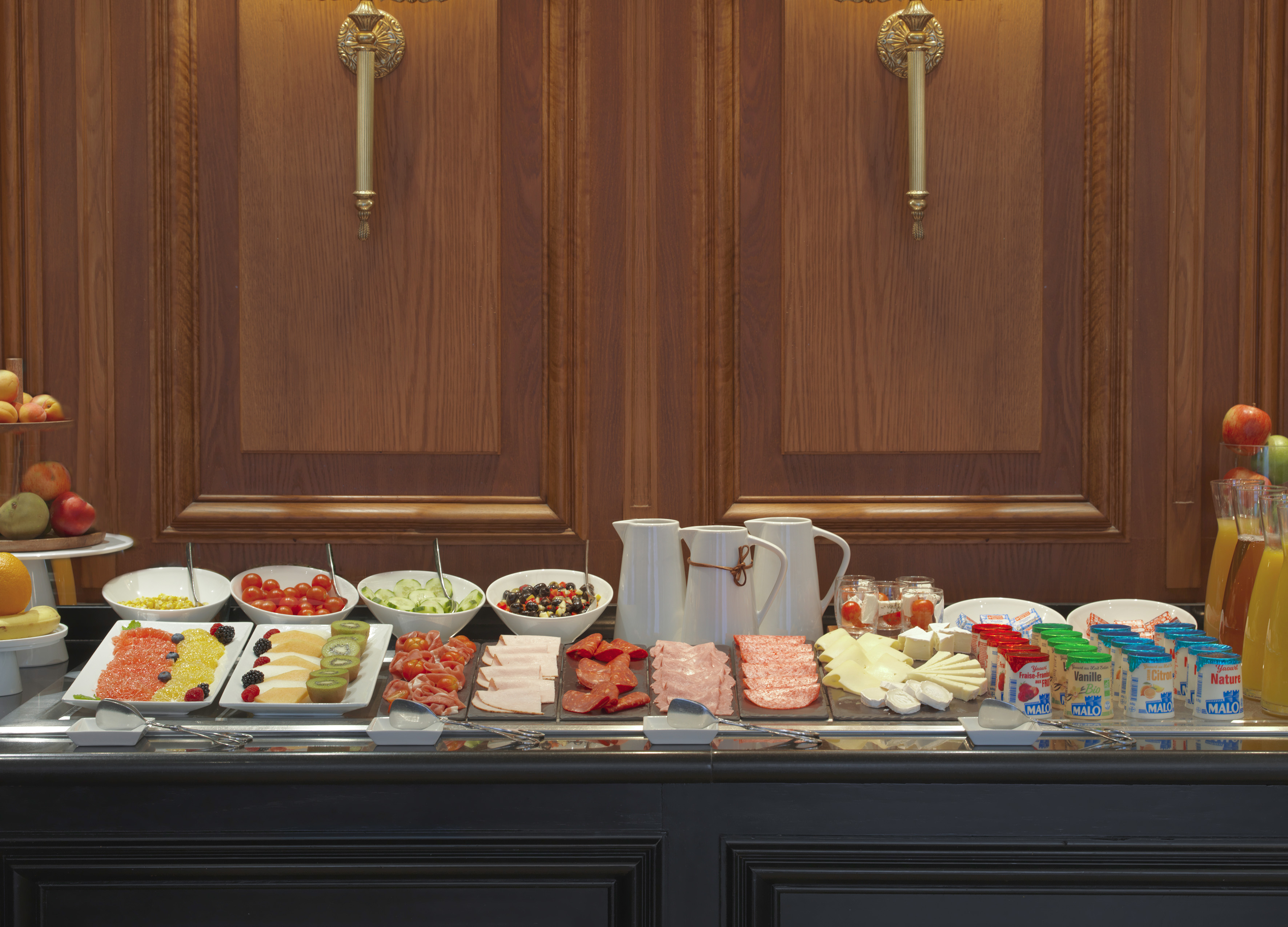 Hotel breakfast buffet with fresh fruits, cold meats, cheeses, yogurts, and juices.
