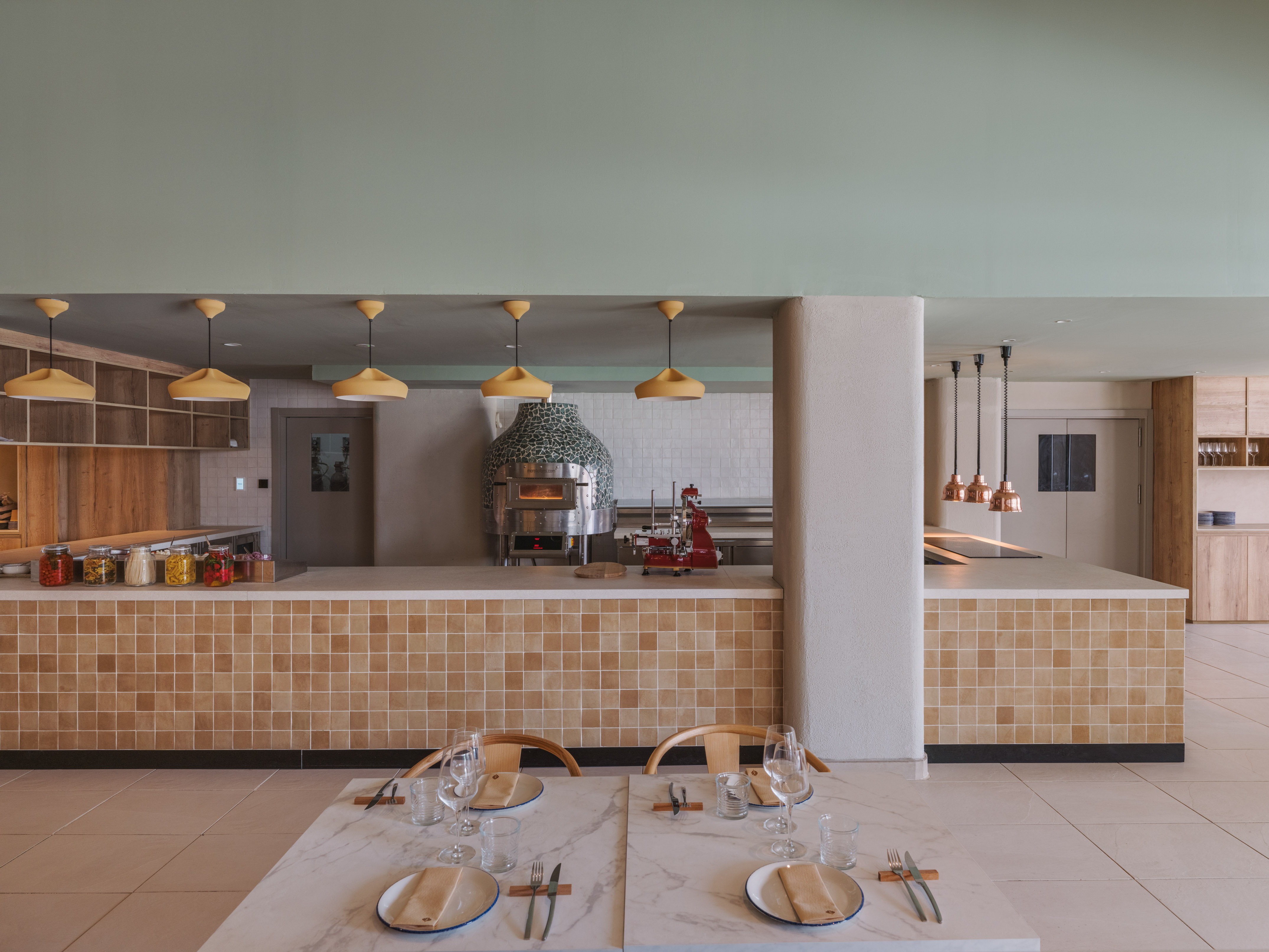 Modern restaurant interior with open kitchen, tiled pizza oven, and set dining tables.