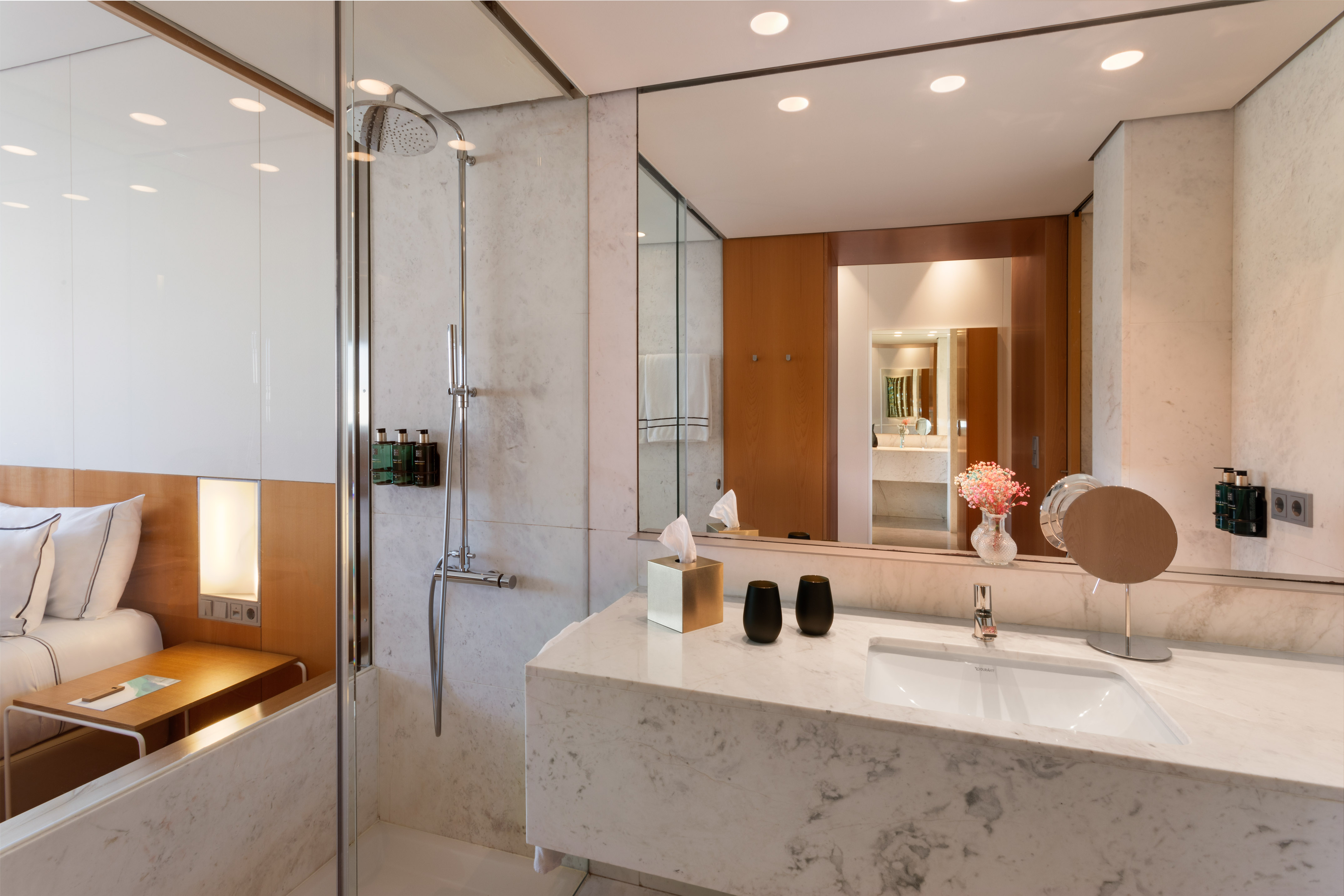 Modern hotel bathroom with marble vanity, undermount sink, and glass shower.