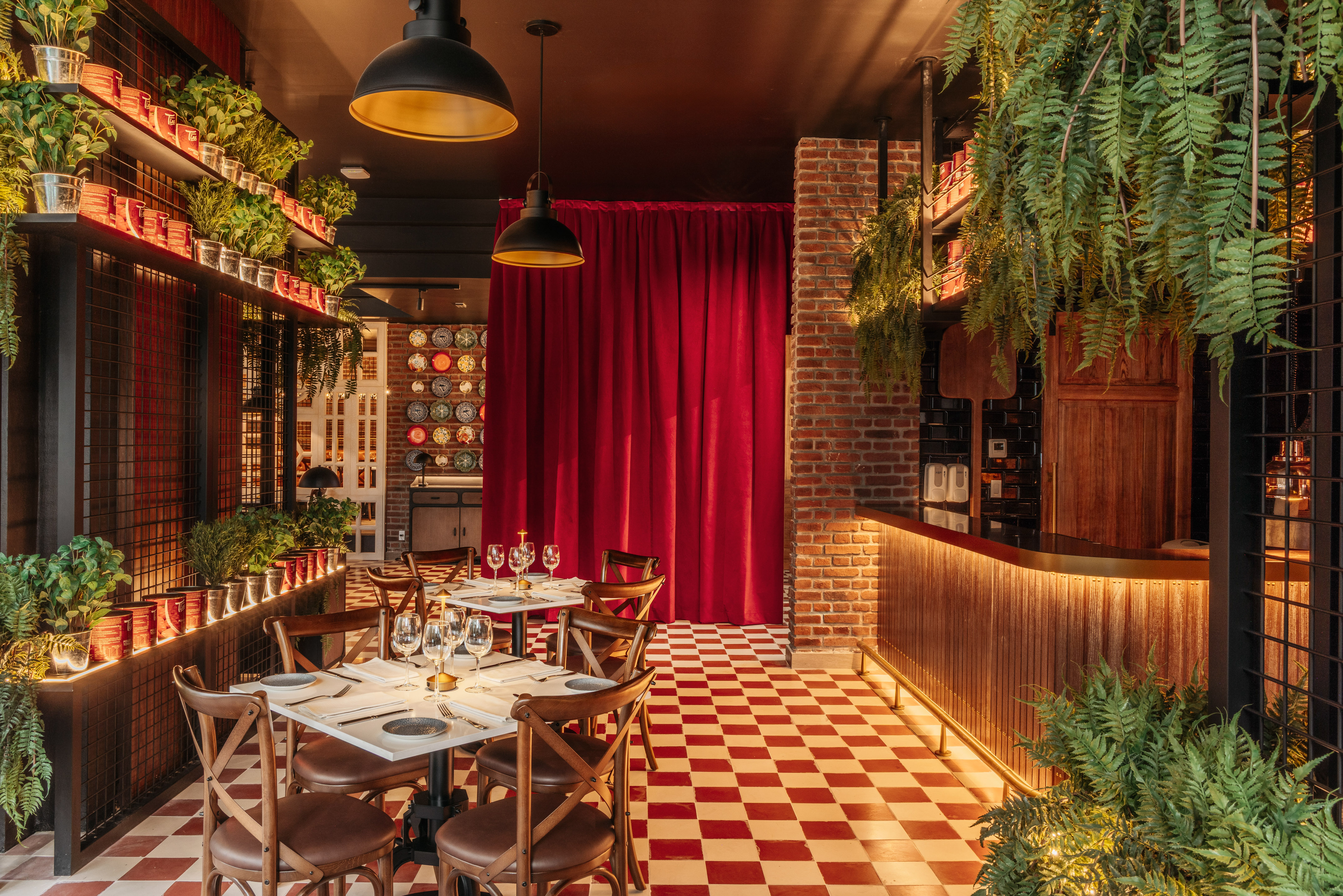 Restaurant interior with red checkered floor, green plants, brick, and dining tables.
