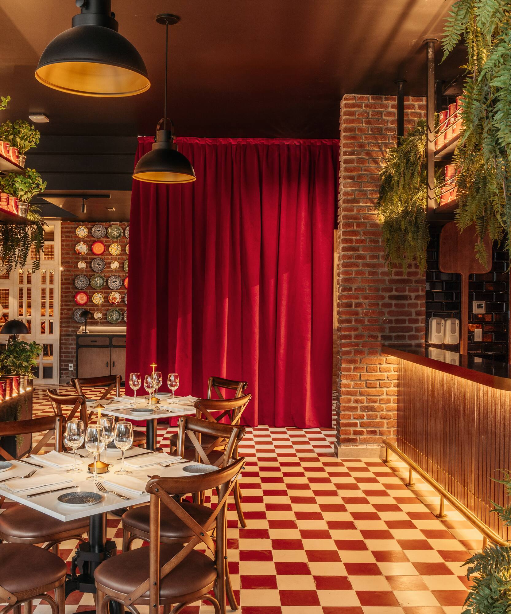 Restaurant interior with red checkered floor, green plants, brick, and dining tables.