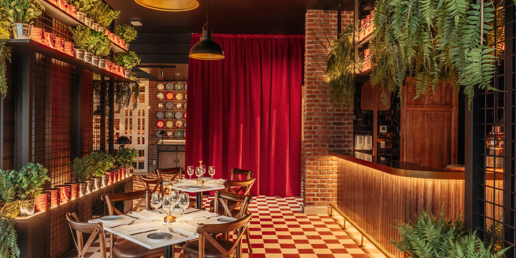 Restaurant interior with red checkered floor, green plants, brick, and dining tables.