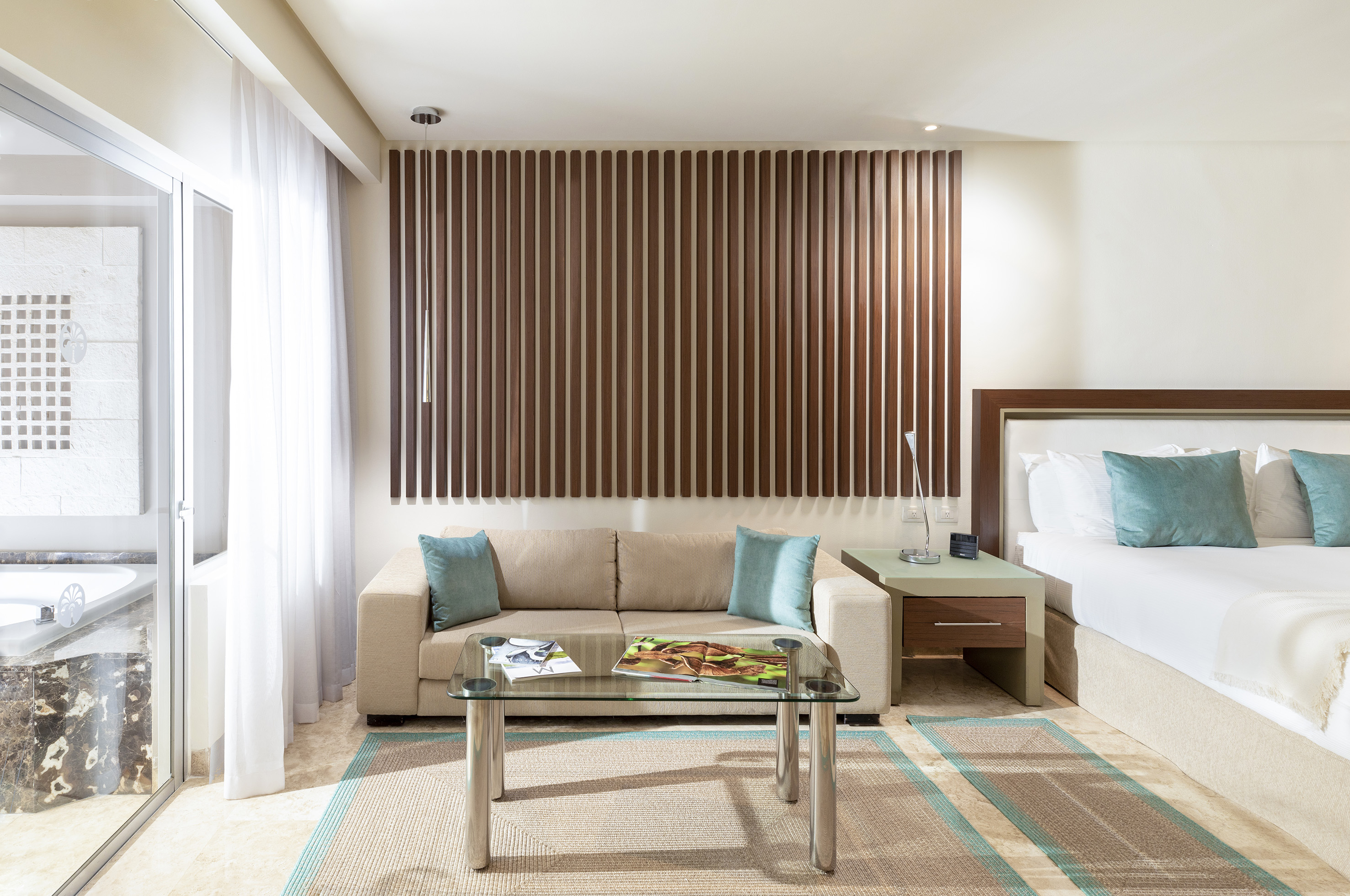 Luxury hotel suite with bed, beige sofa, wood slat wall, and patio access.