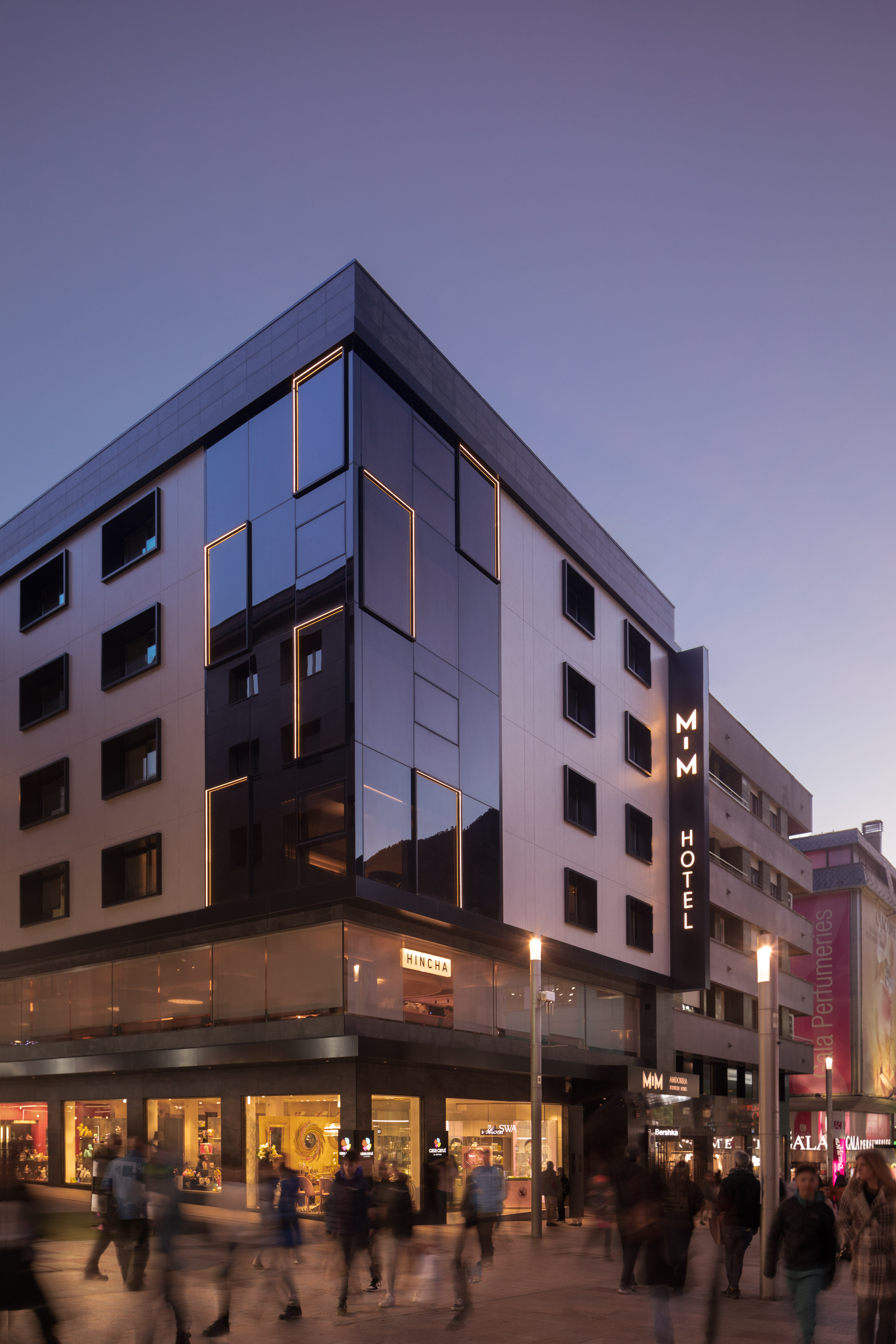 MIM Hotel Andorra, modern glass building with illuminated facade at twilight.