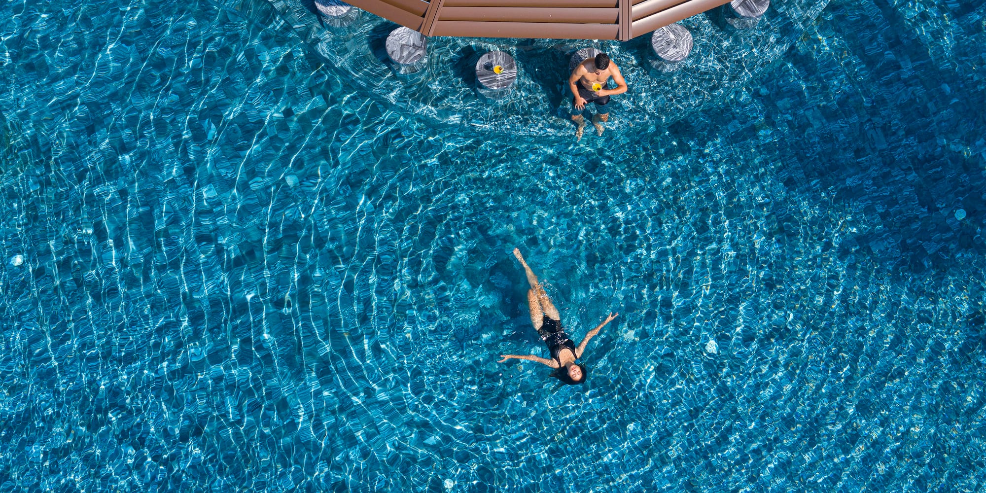 Aerial view of man at swim-up bar and woman floating in resort pool.