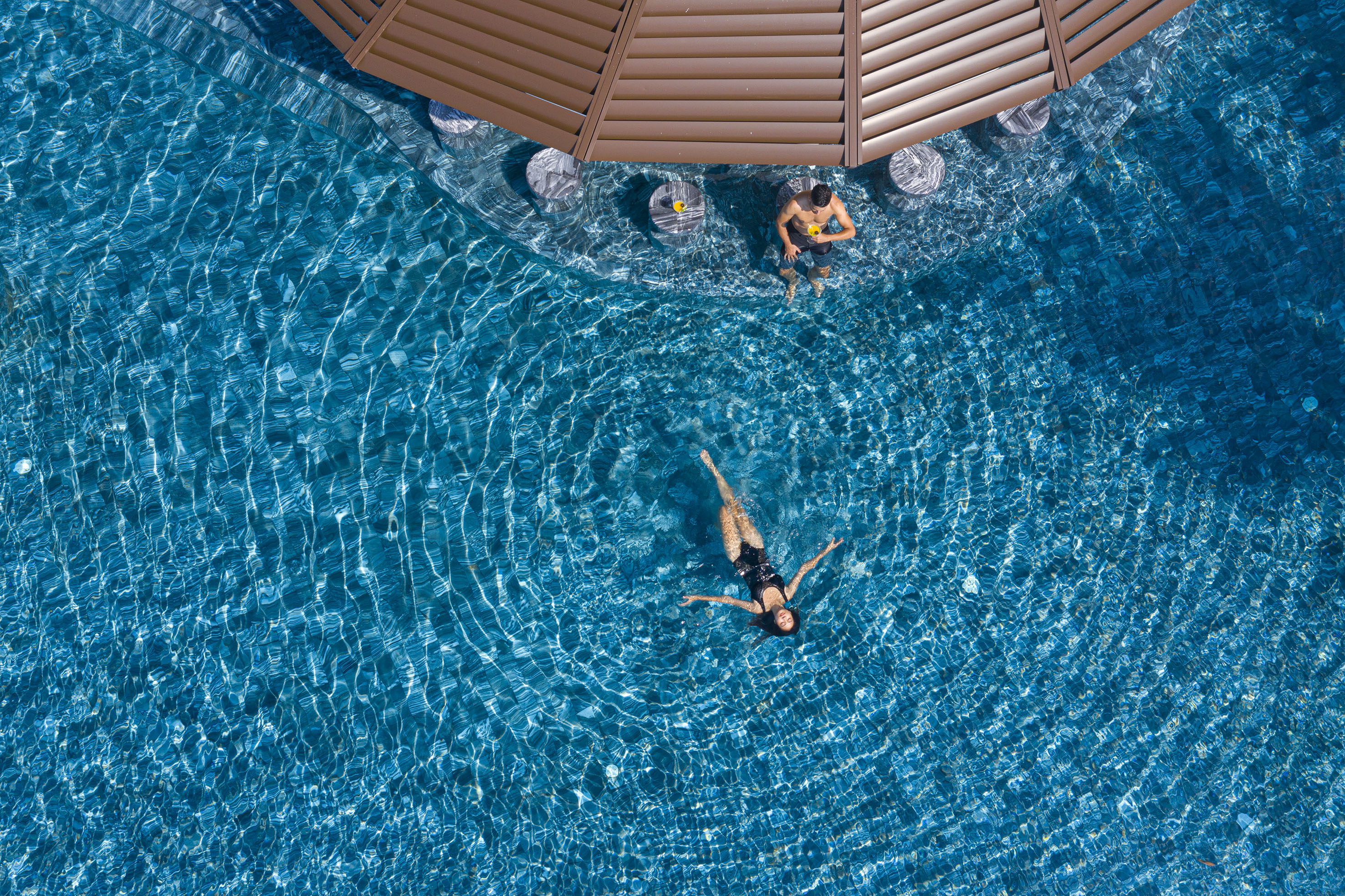 Aerial view of man at swim-up bar and woman floating in resort pool.