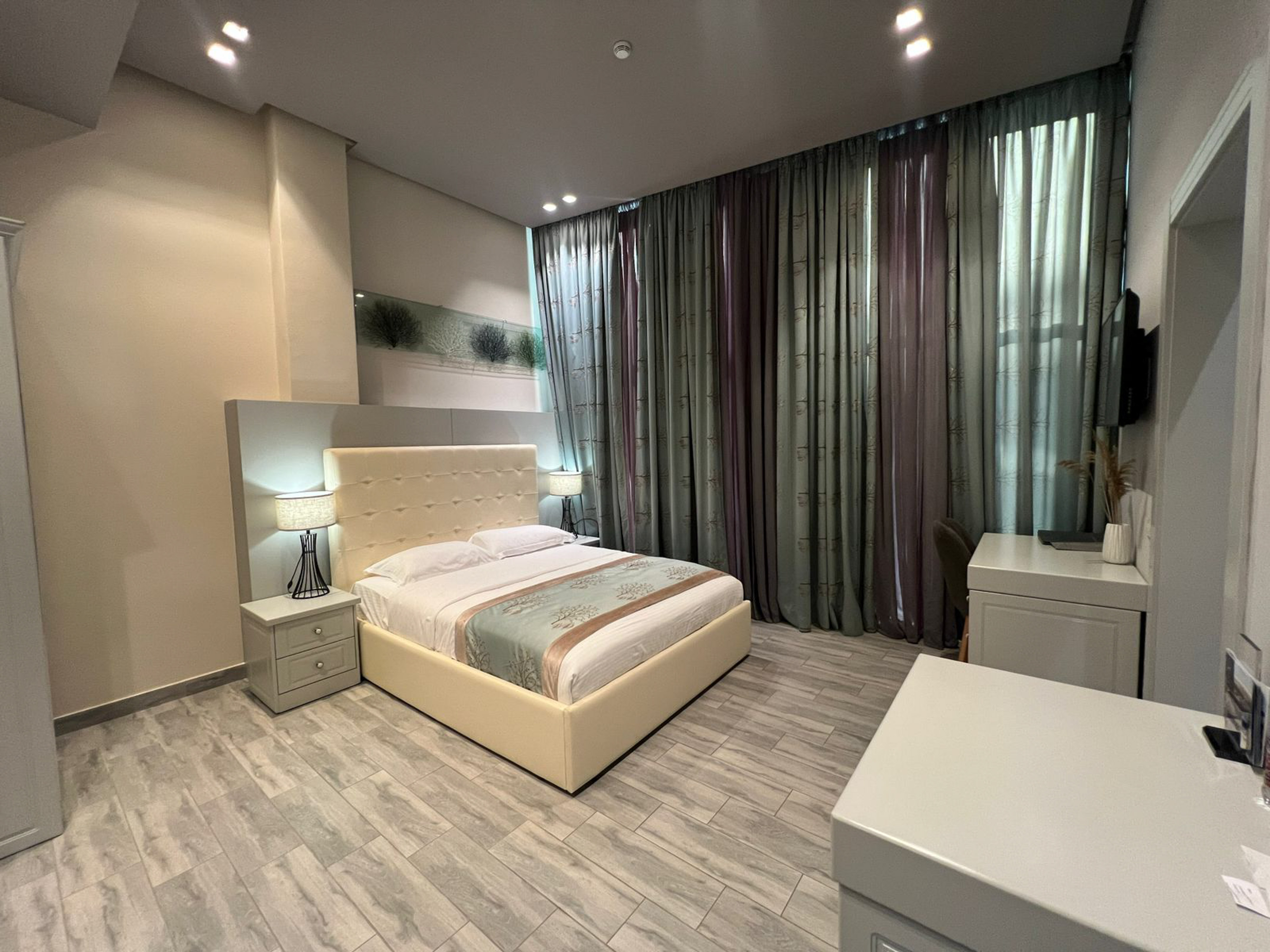 Modern hotel bedroom with comfortable bed, grey wood floor, and dark curtains.