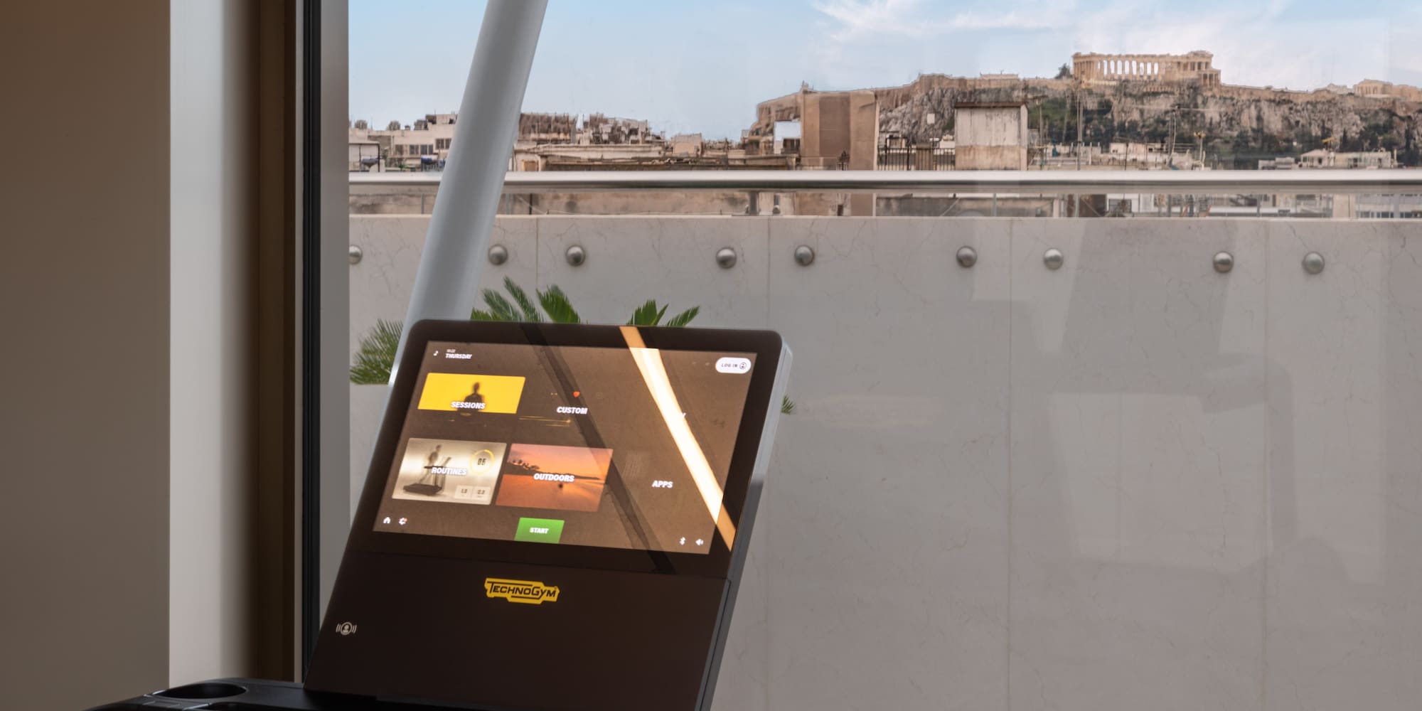 Technogym treadmill screen showing fitness programs, overlooking Athens Acropolis.