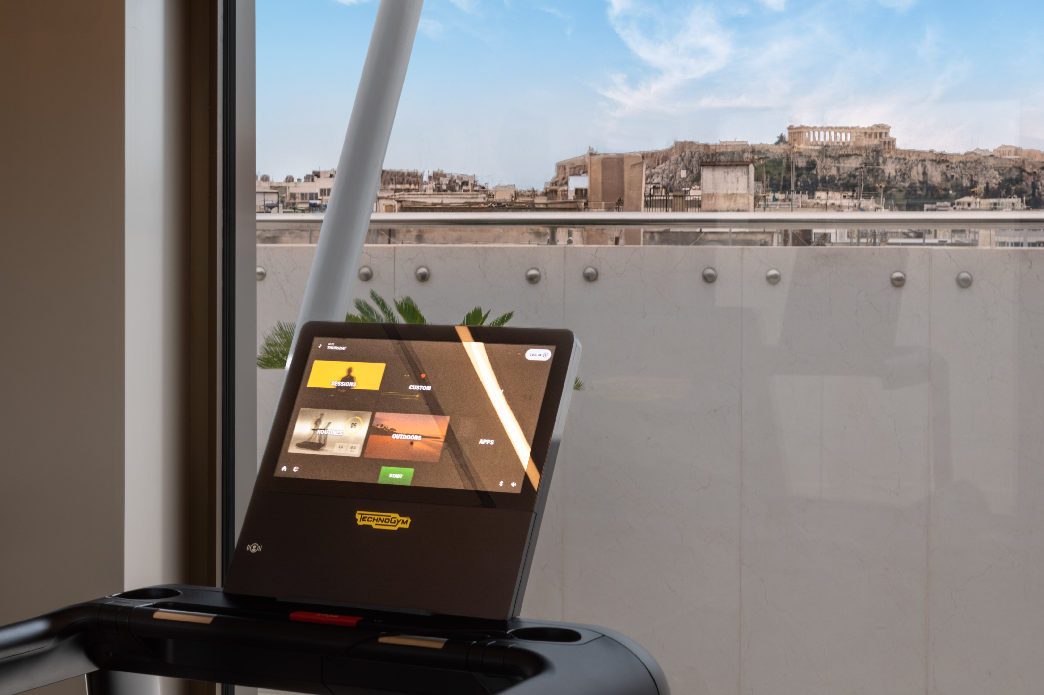 Technogym treadmill screen showing fitness programs, overlooking Athens Acropolis.