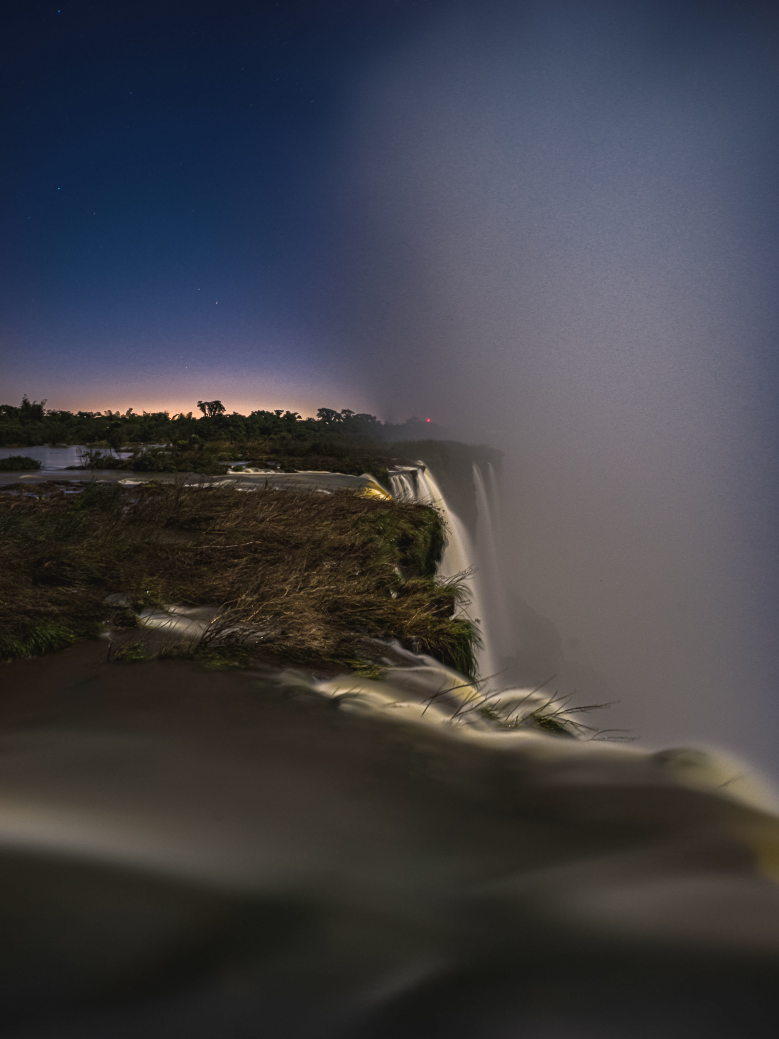 Misty waterfall at night, long exposure water, starry sky, and jungle.