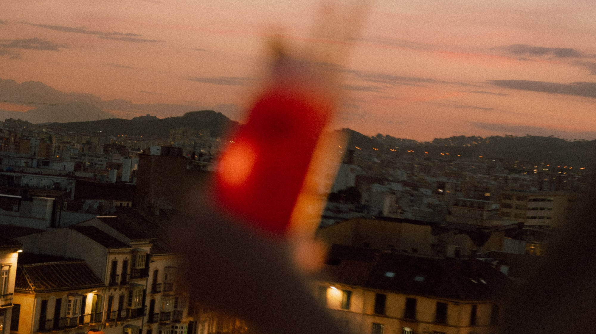 Cityscape at dusk with illuminated buildings and blurry red foreground.