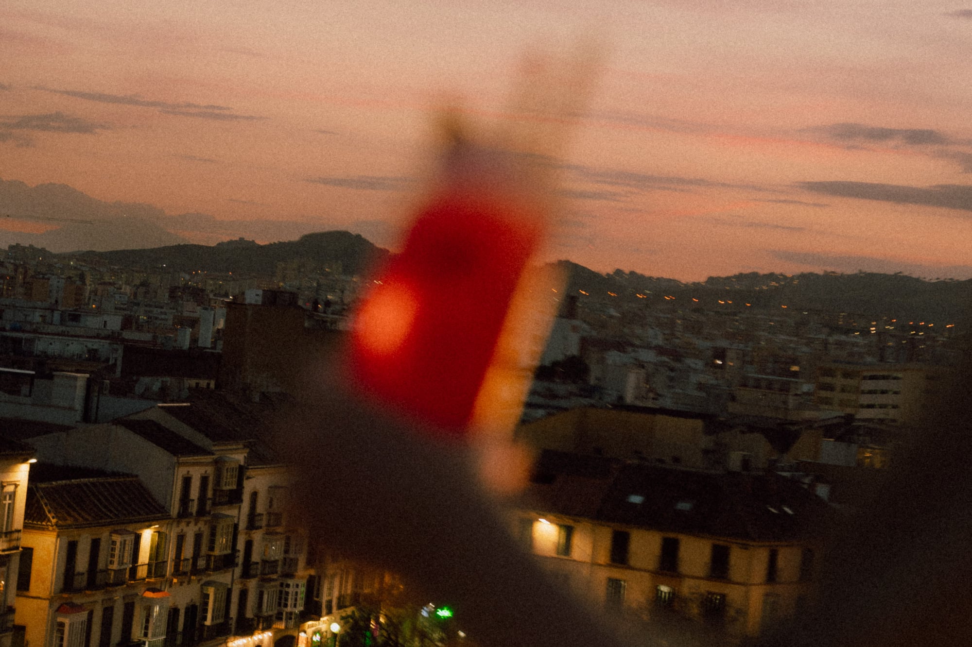 Cityscape at dusk with illuminated buildings and blurry red foreground.