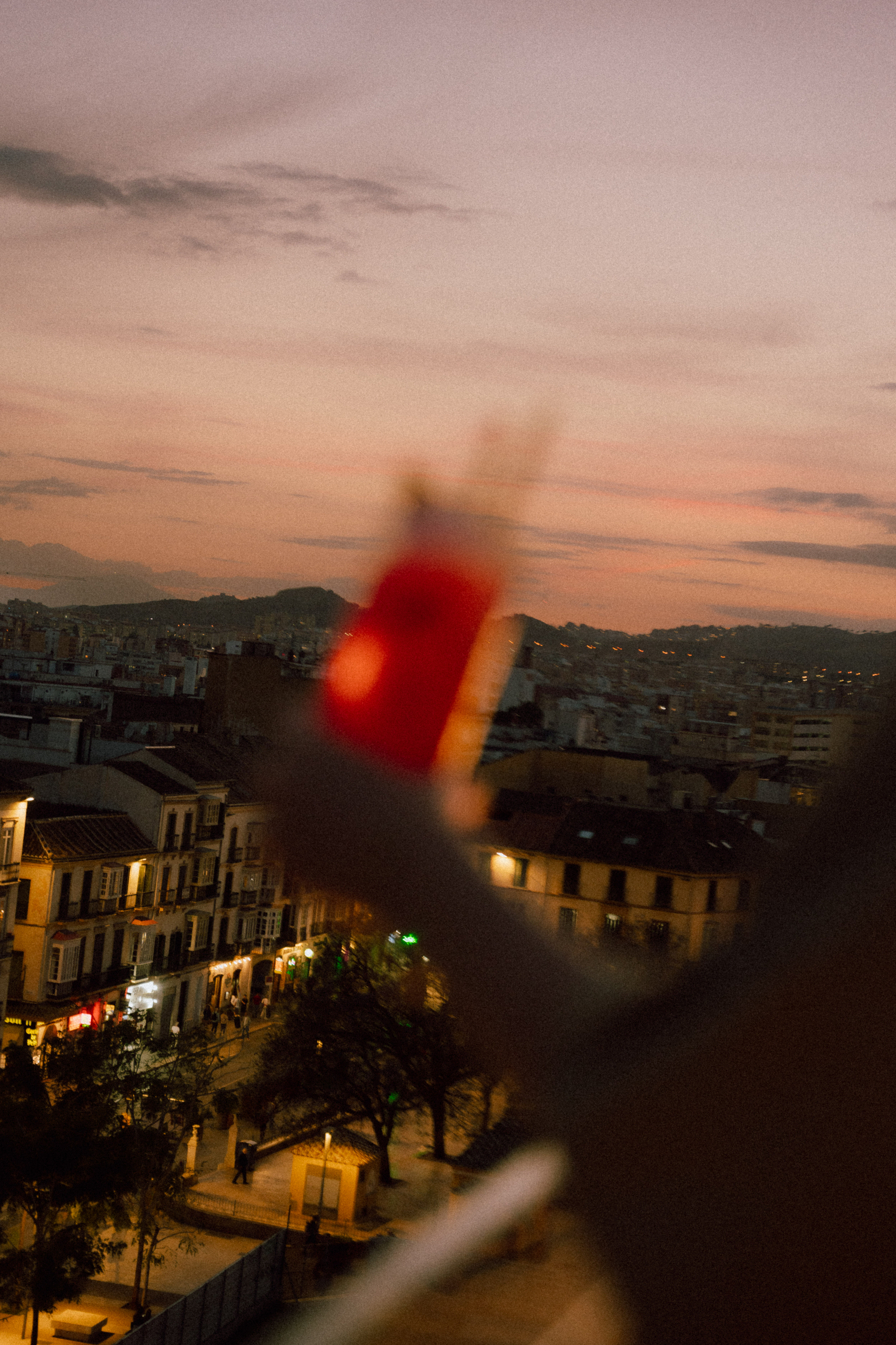 Cityscape at dusk with illuminated buildings and blurry red foreground.