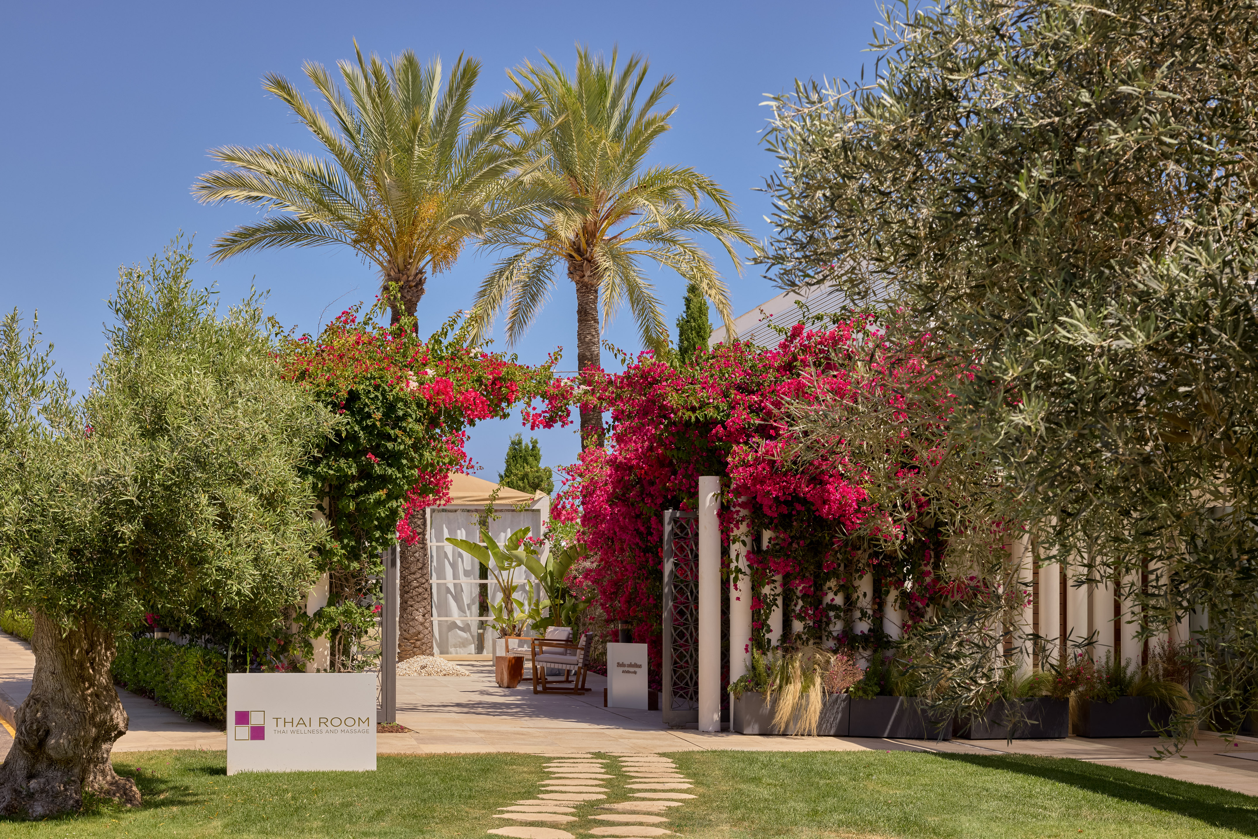 Lush tropical entrance to Thai Room spa with pink bougainvillea and palm trees.