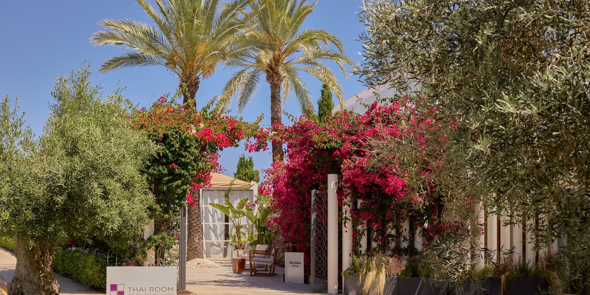 Lush tropical entrance to Thai Room spa with pink bougainvillea and palm trees.