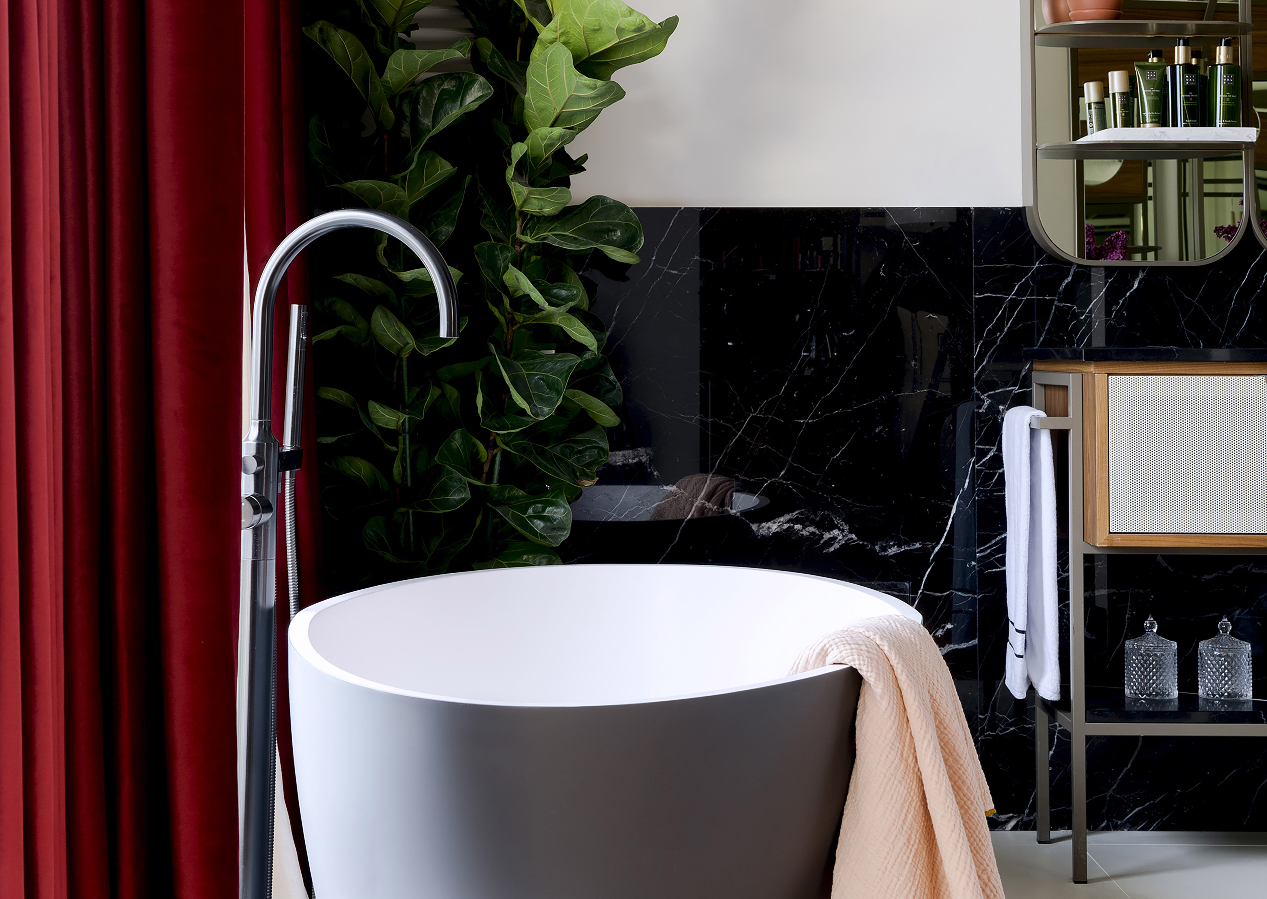 Modern bathroom: freestanding tub, chrome faucet, black marble, red curtain.