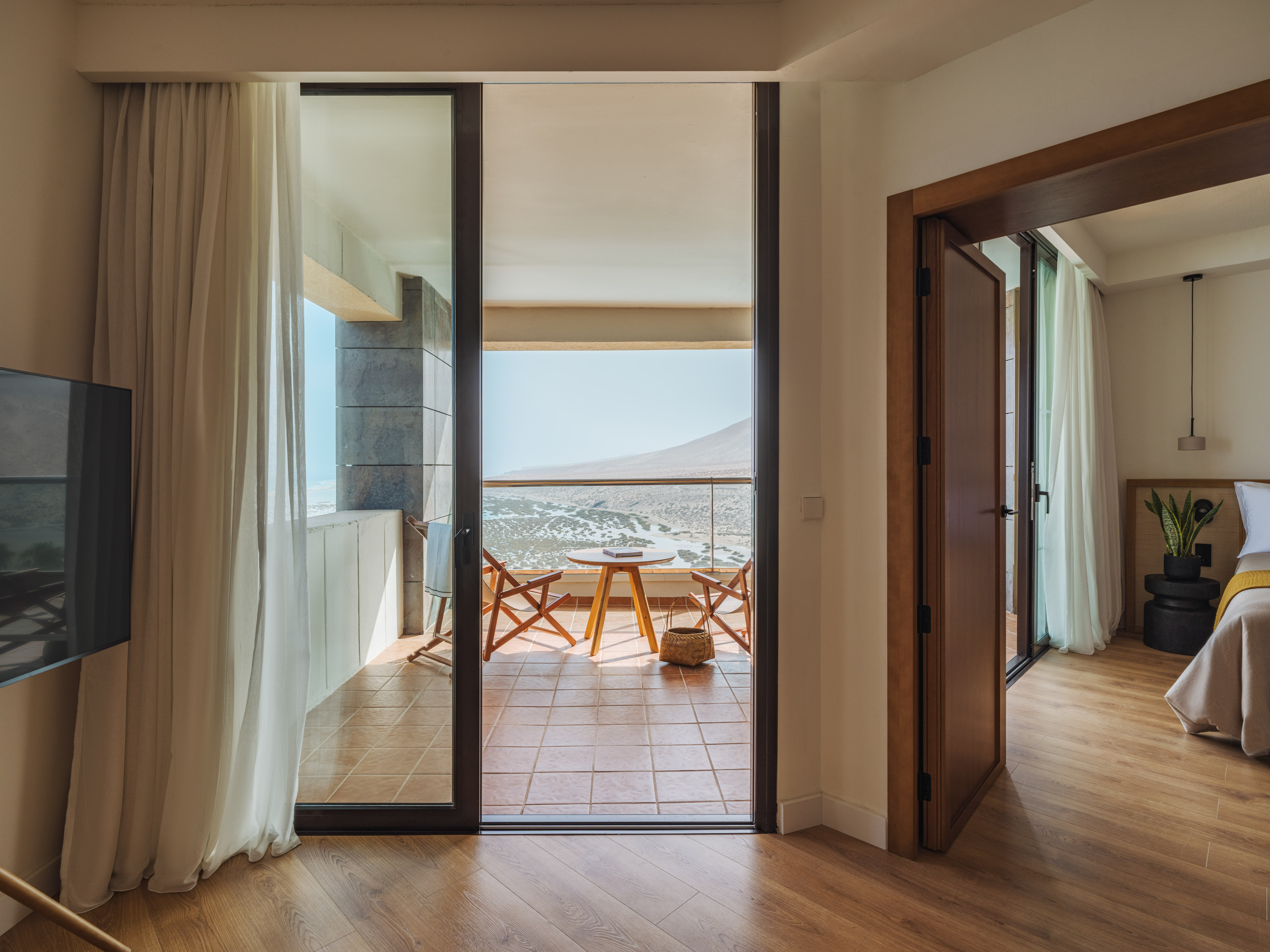 Modern hotel bedroom with balcony, desert landscape view, and outdoor seating.