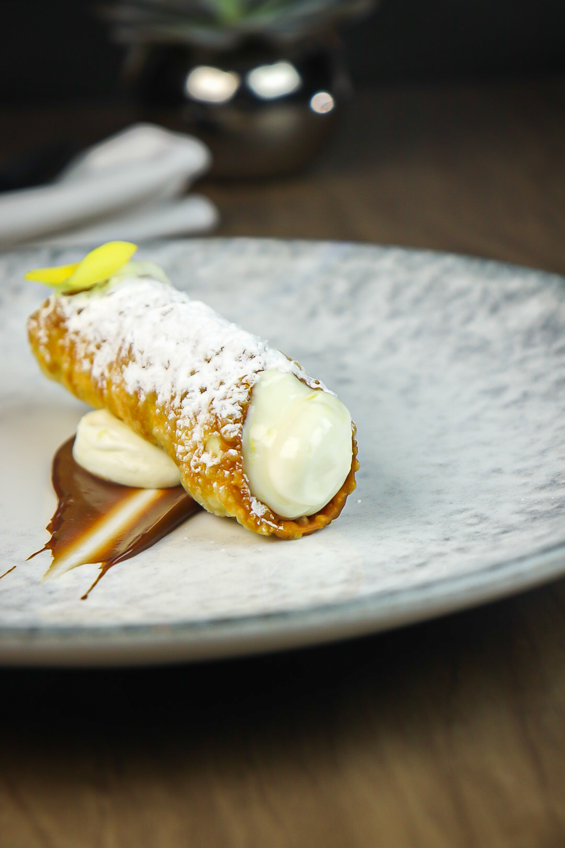 Cannoli with powdered sugar, white cream filling, chocolate sauce, yellow garnish.