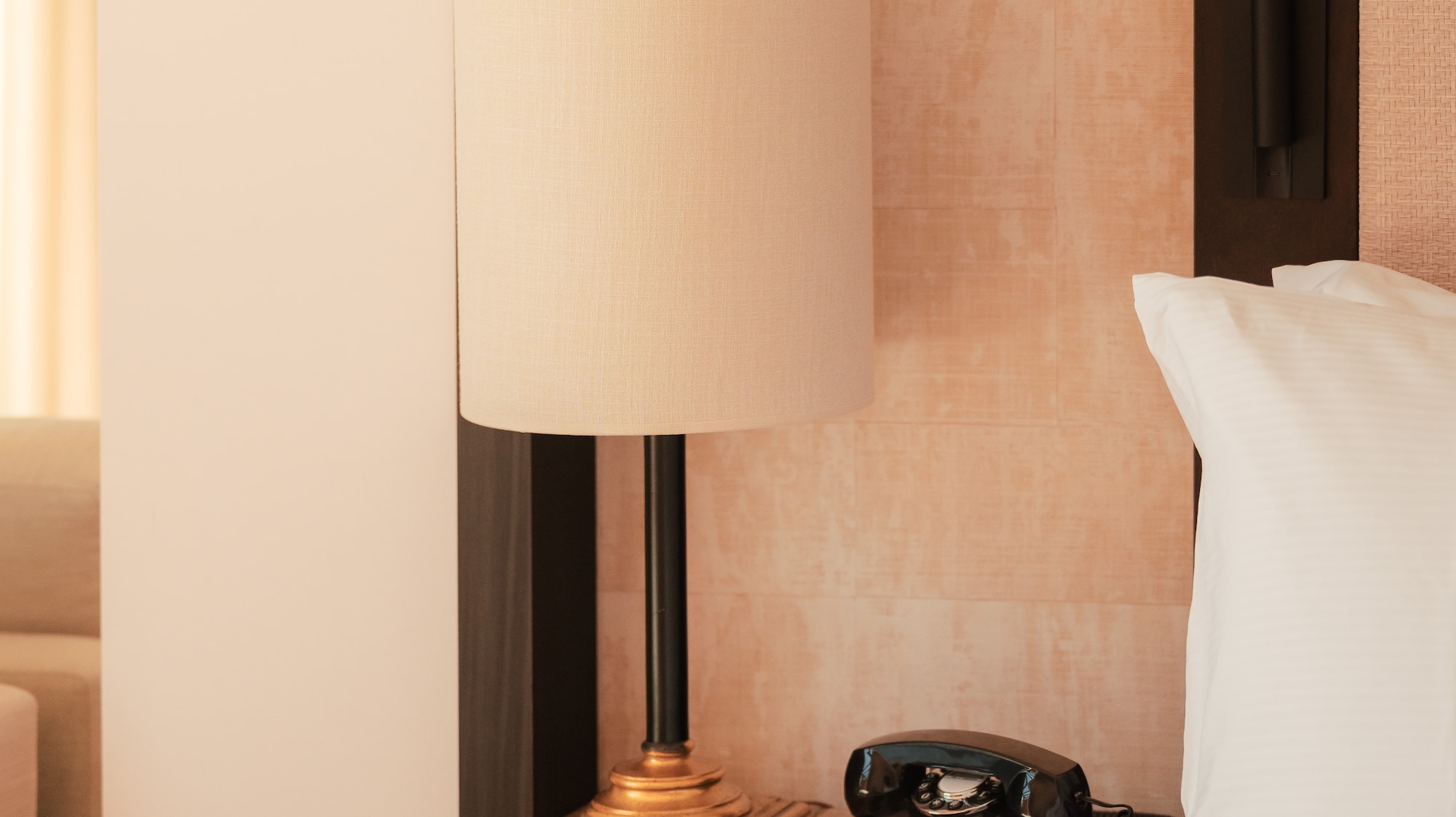 Hotel room nightstand with lamp, vintage rotary phone, and white bedding.