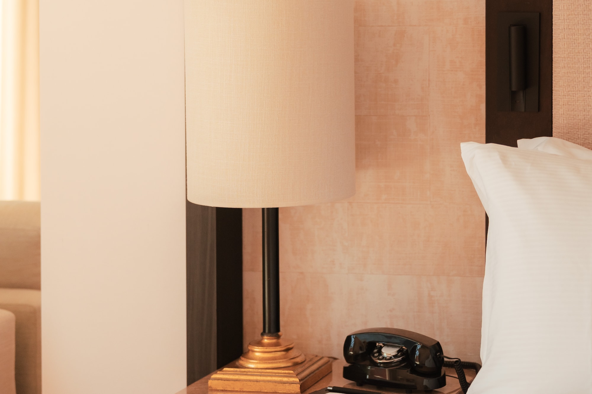 Hotel room nightstand with lamp, vintage rotary phone, and white bedding.