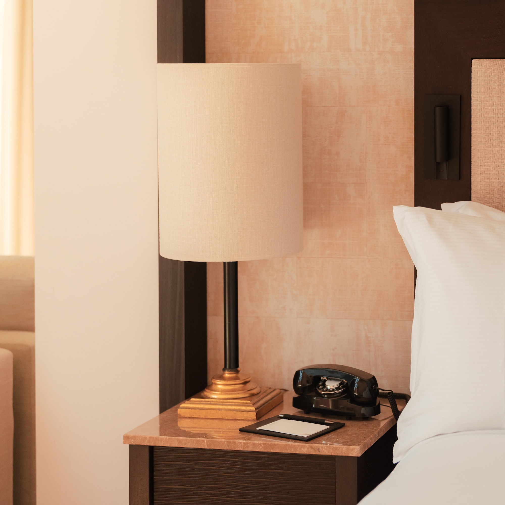 Hotel room nightstand with lamp, vintage rotary phone, and white bedding.