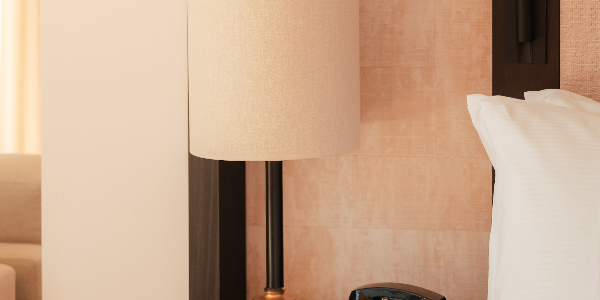 Hotel room nightstand with lamp, vintage rotary phone, and white bedding.