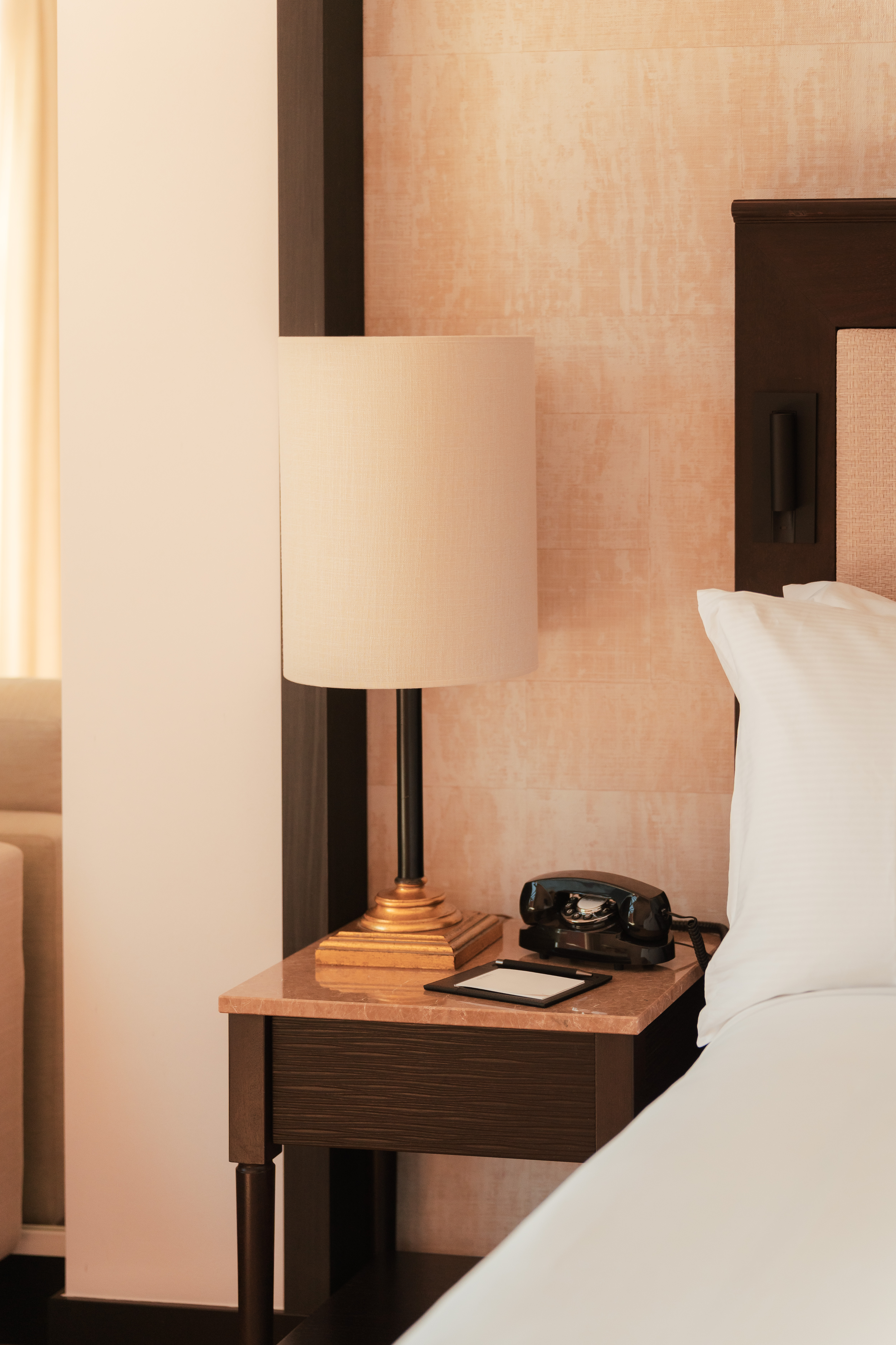 Hotel room nightstand with lamp, vintage rotary phone, and white bedding.