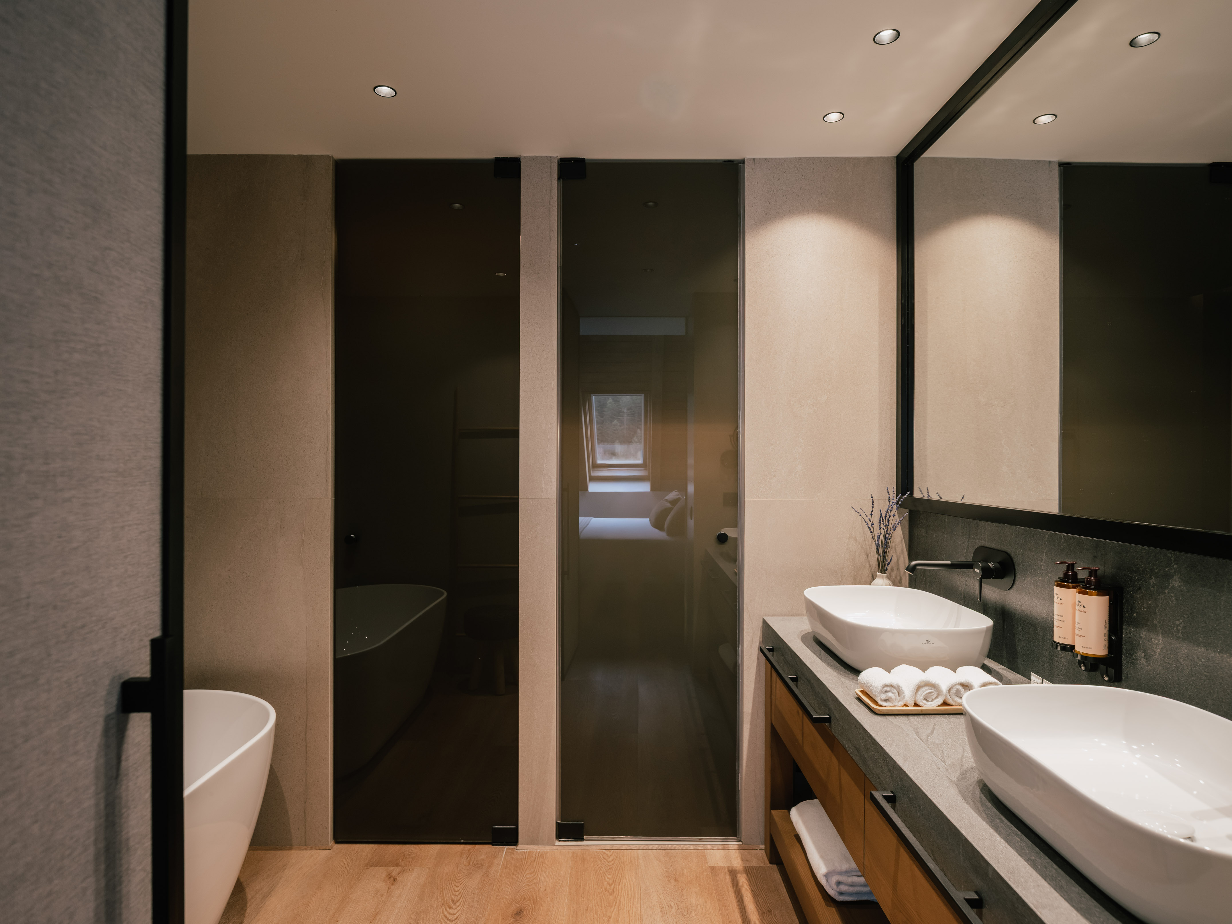 Sleek bathroom: freestanding tub, double vessel sinks, dark glass shower, wood floor.