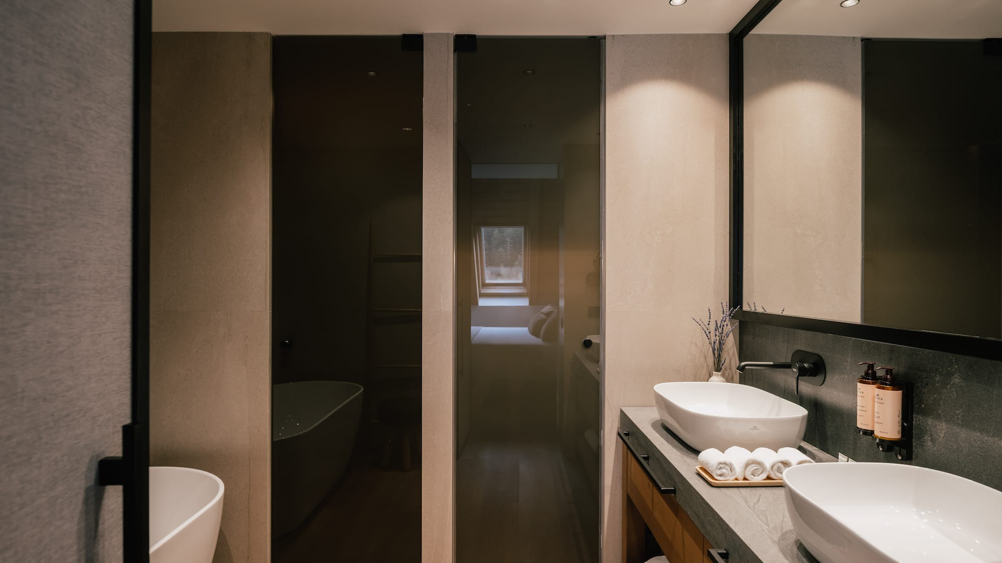 Sleek bathroom: freestanding tub, double vessel sinks, dark glass shower, wood floor.