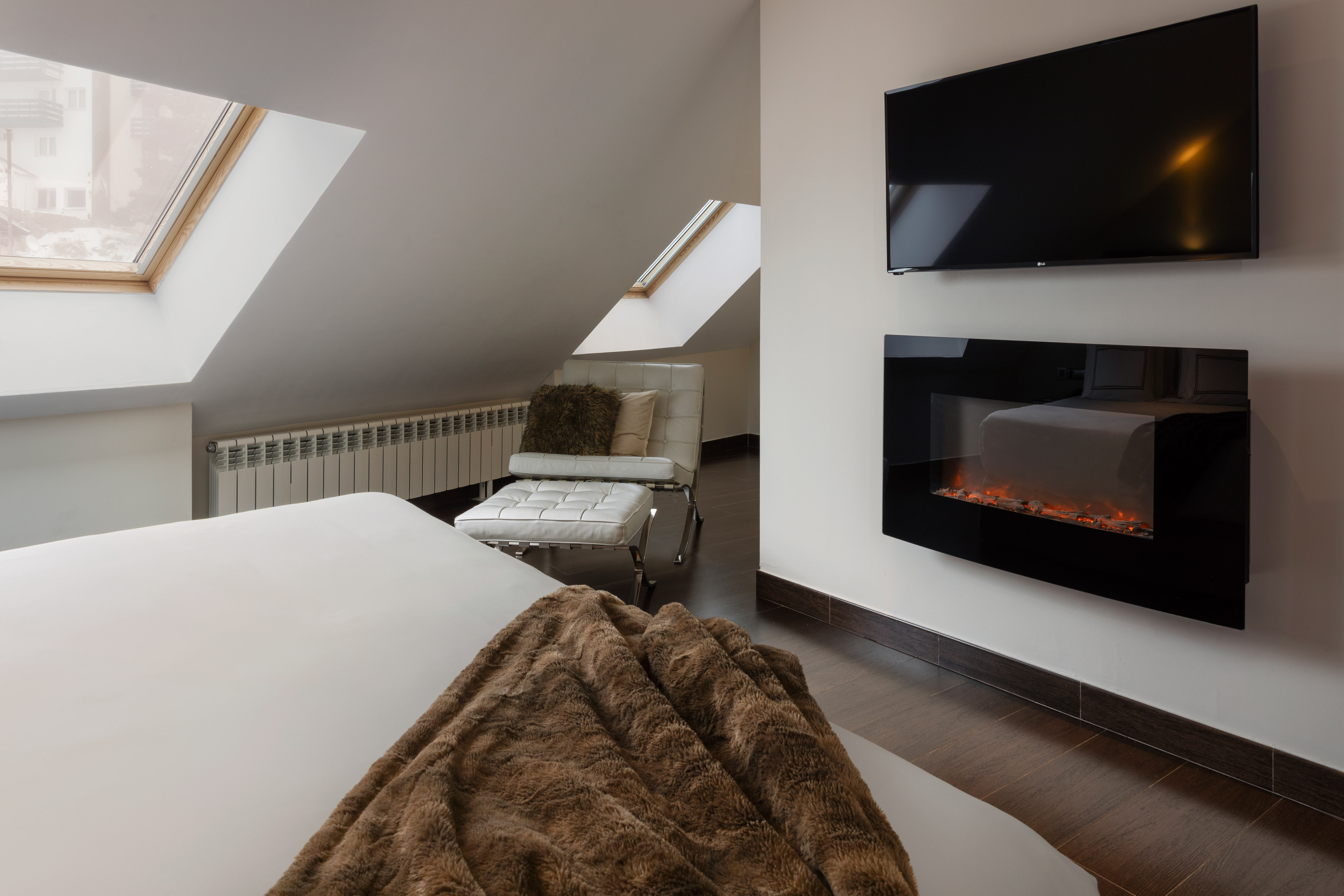 Modern loft bedroom with skylights, electric fireplace, and TV.
