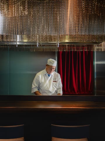 a man in a chef's hat standing in a room with chairs and a red curtain