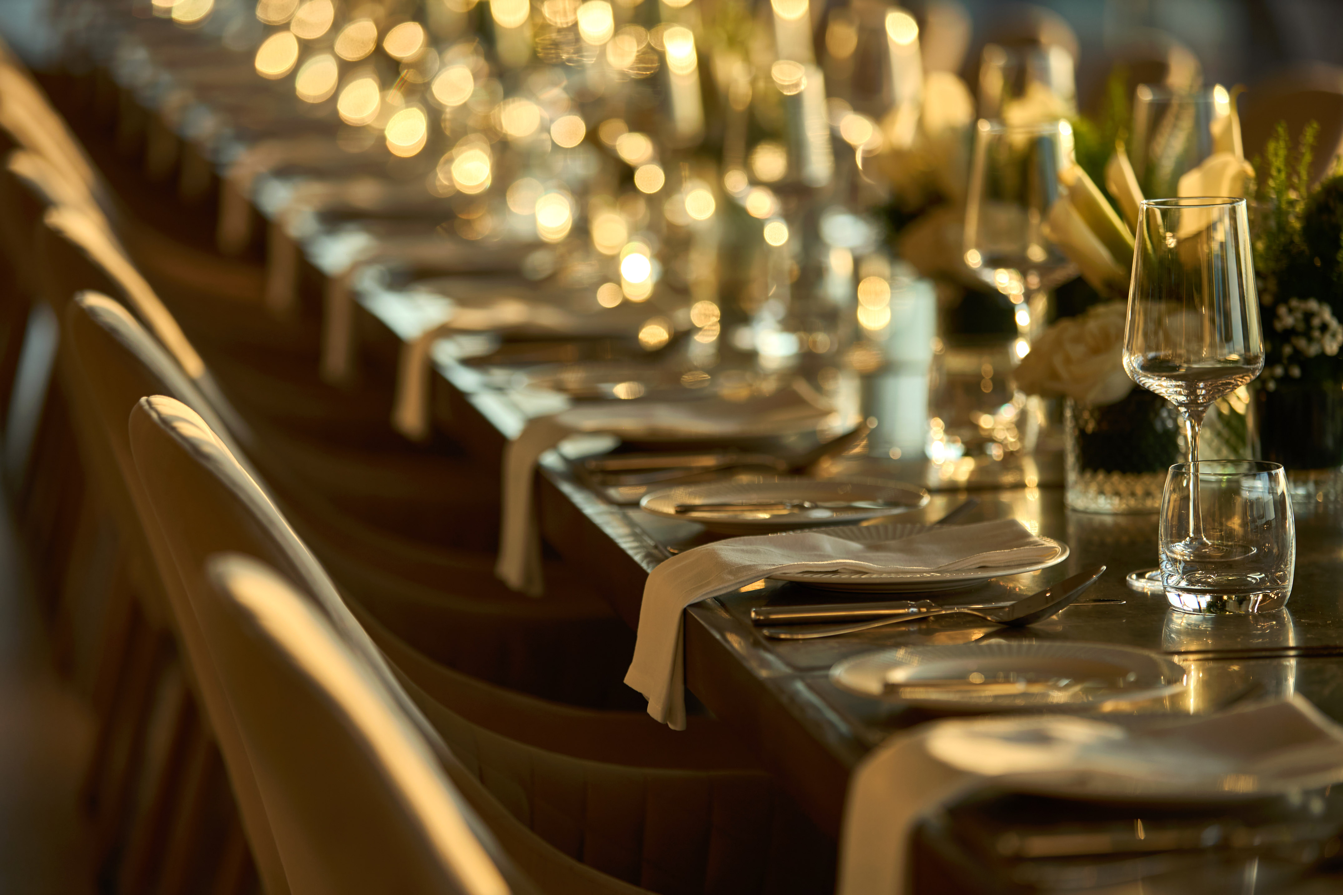 Elegant dining table set with place settings, glassware, and warm event lighting.