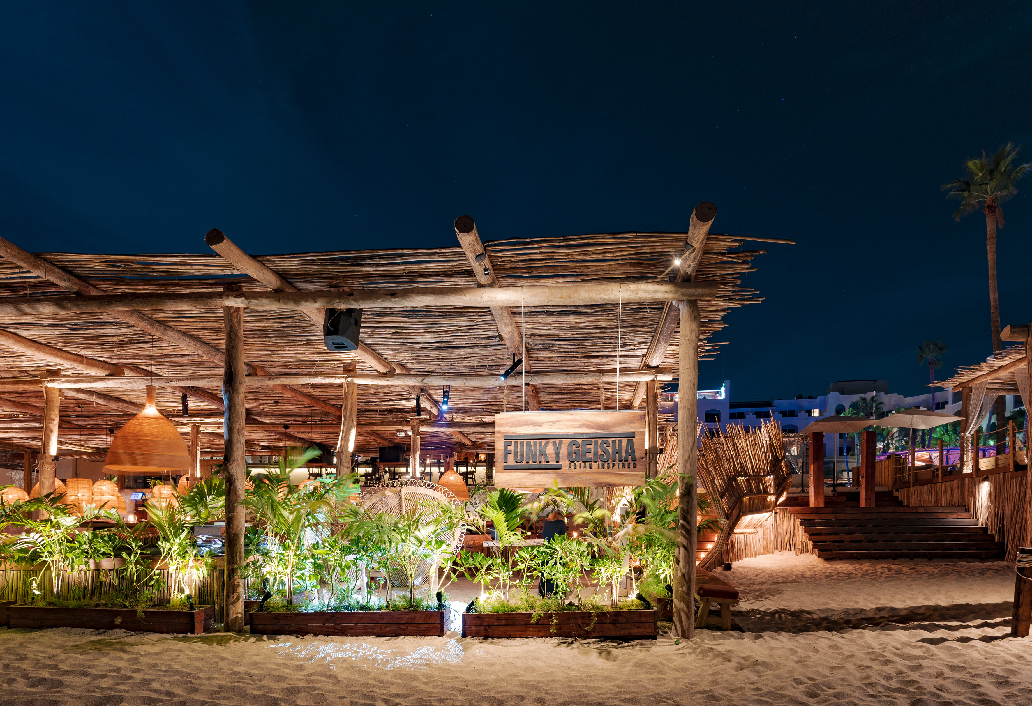 Funky Geisha Asian Inspired outdoor beach restaurant at night, rustic wood, plants.