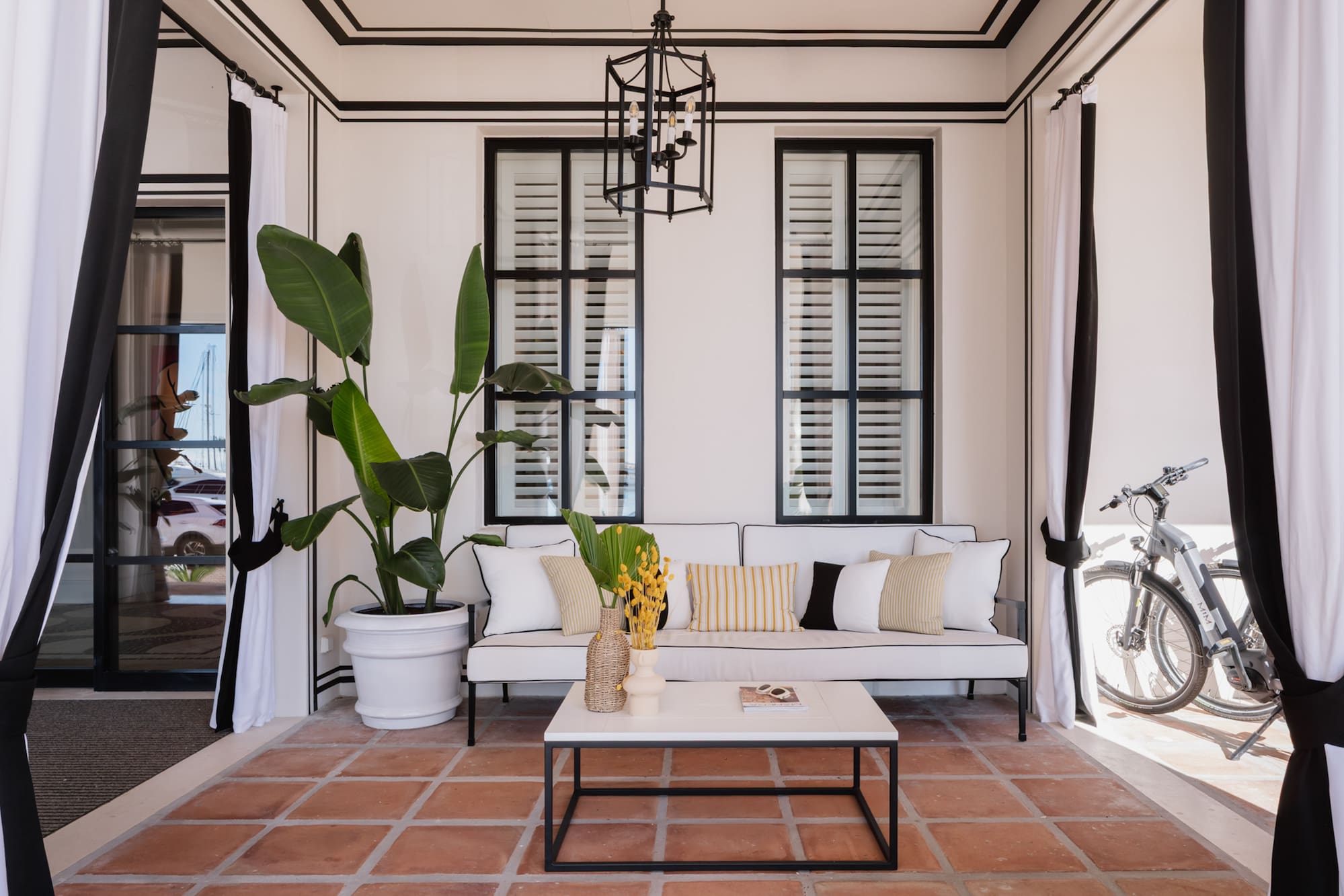 Coastal outdoor lounge with white sofa, black details, terracotta floor.