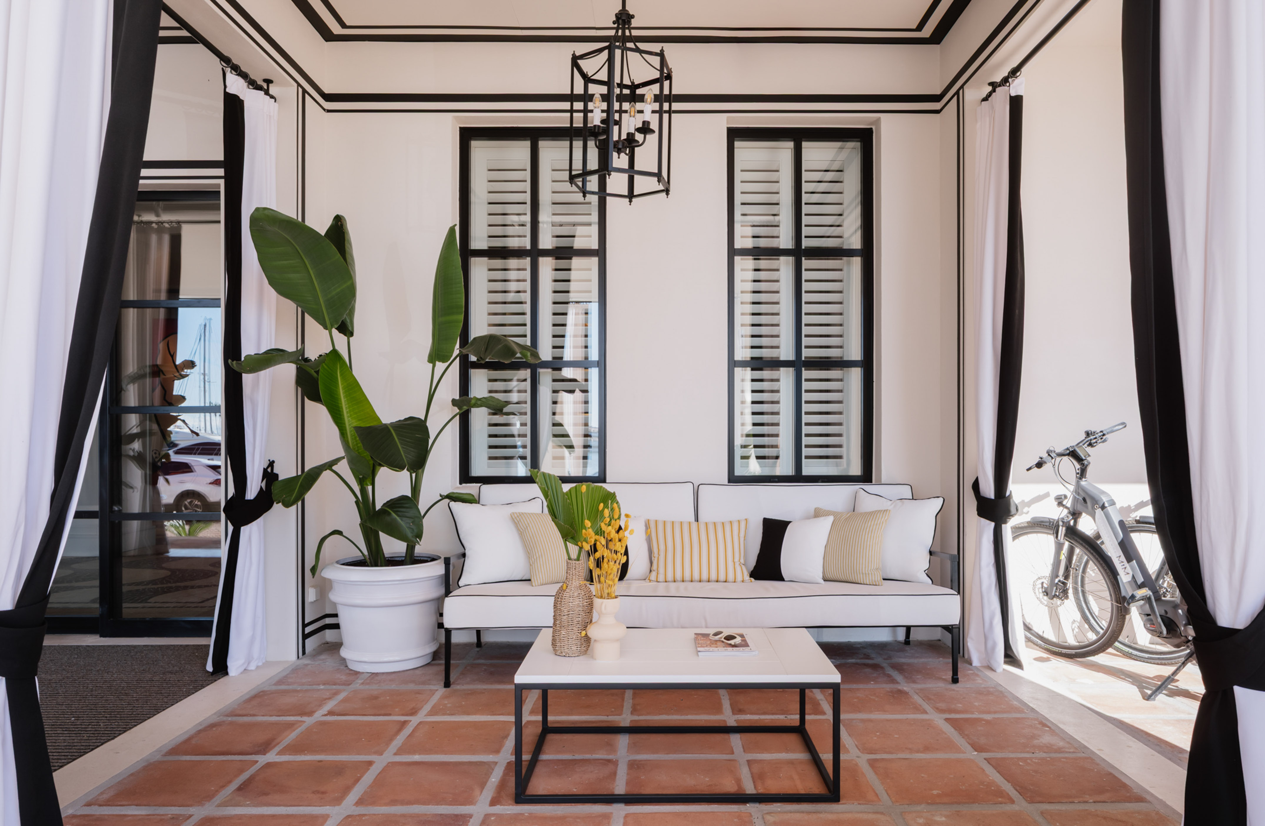 Coastal outdoor lounge with white sofa, black details, terracotta floor.