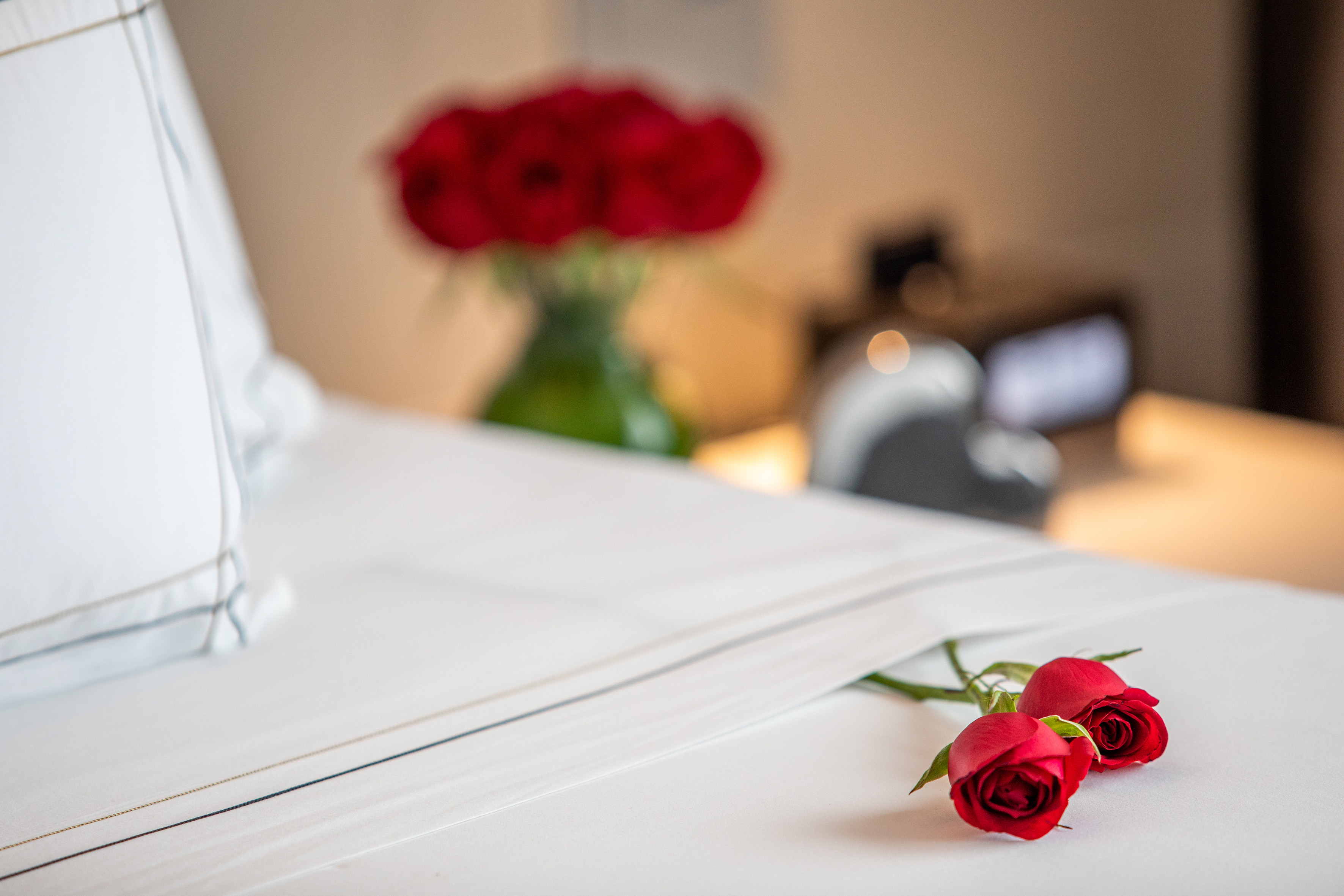 Romantic hotel room with two red roses on white bed linen.