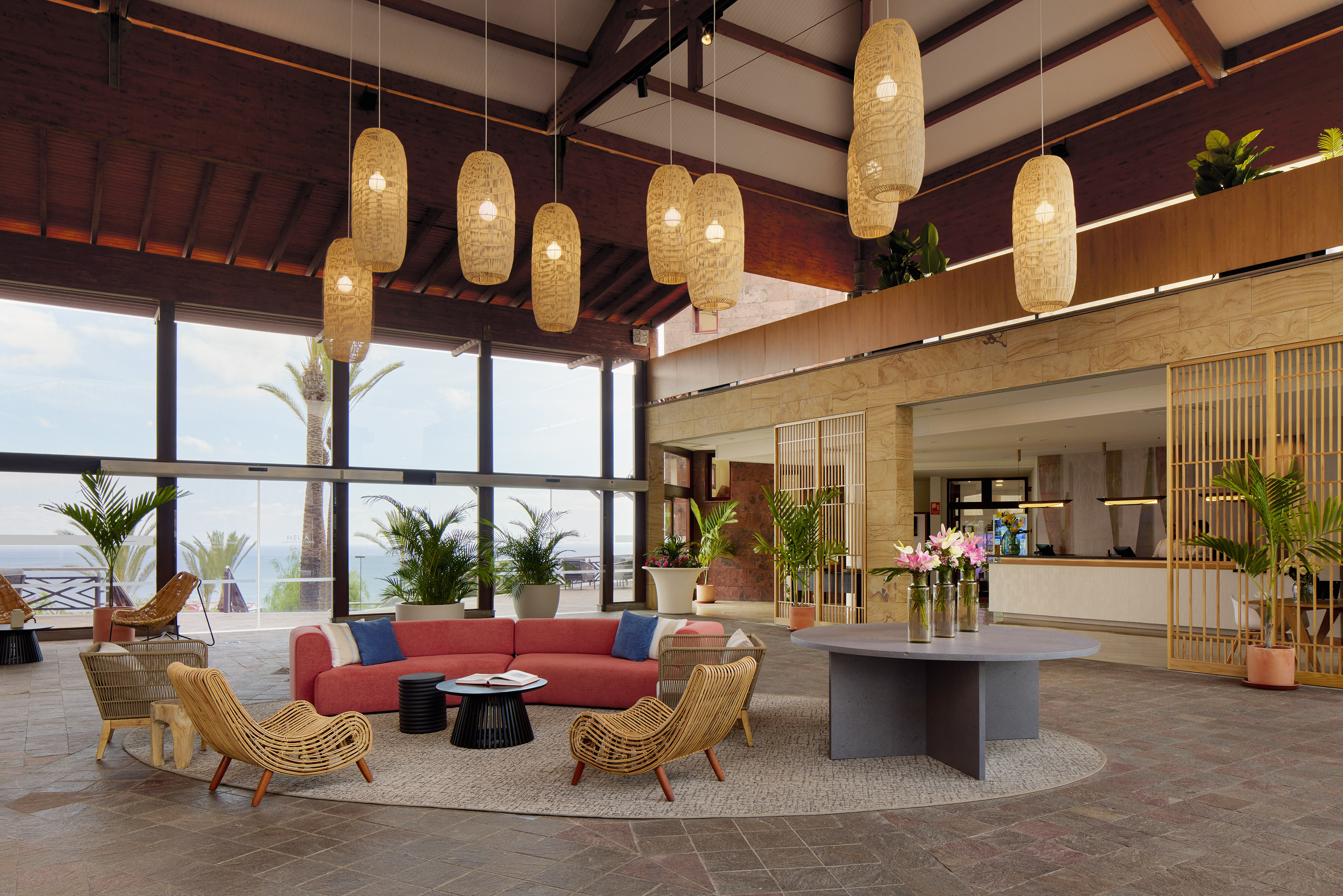 Stylish hotel lobby lounge with red sofa, palm trees, and coastal views.