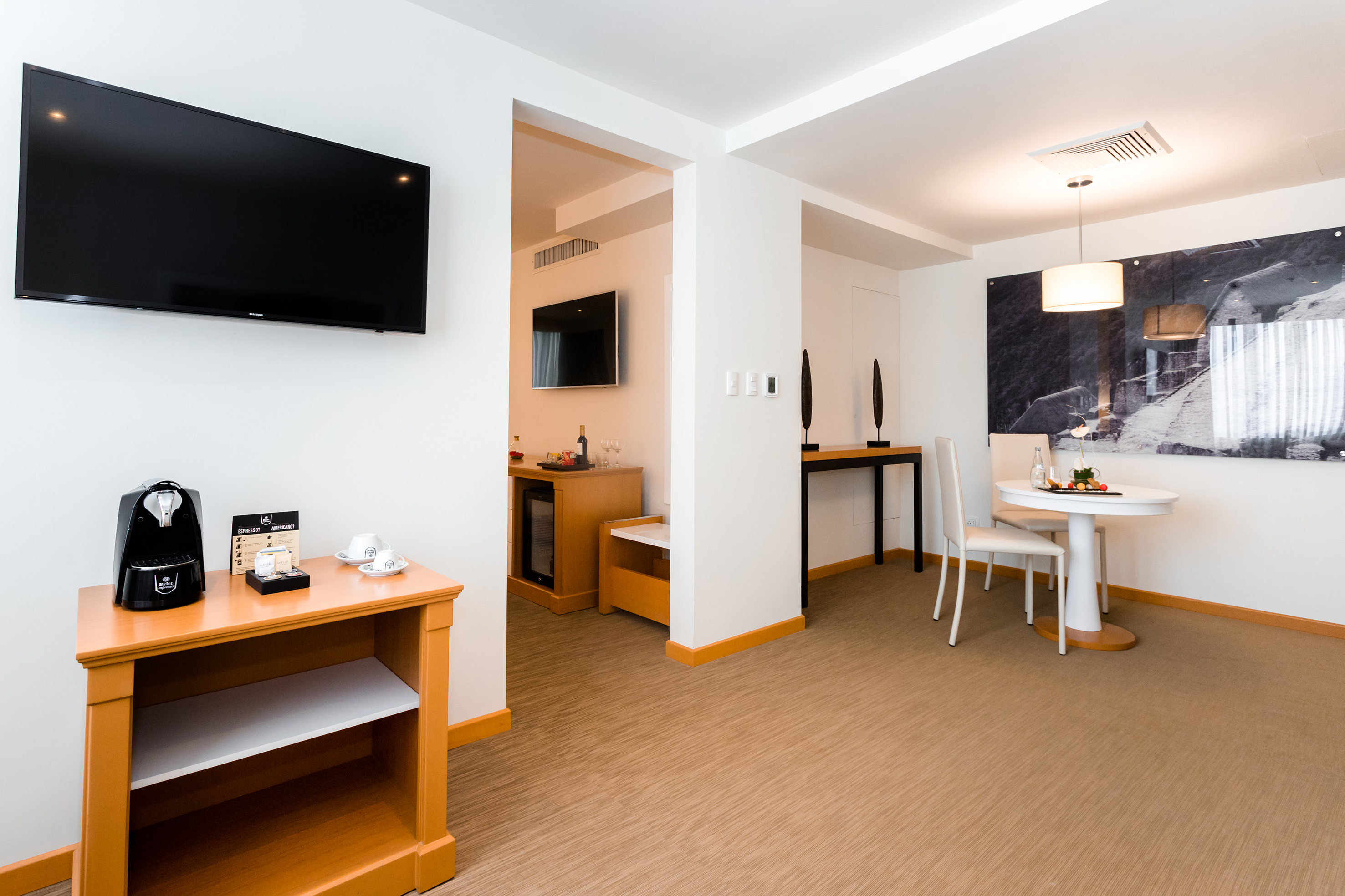 Modern hotel suite living area with flat-screen TV, coffee maker, and dining table.
