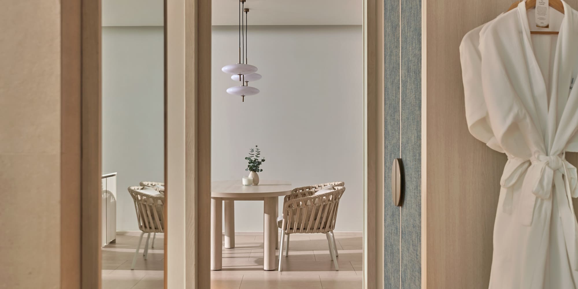 Modern hotel suite: dining area with wicker chairs and hanging robes.
