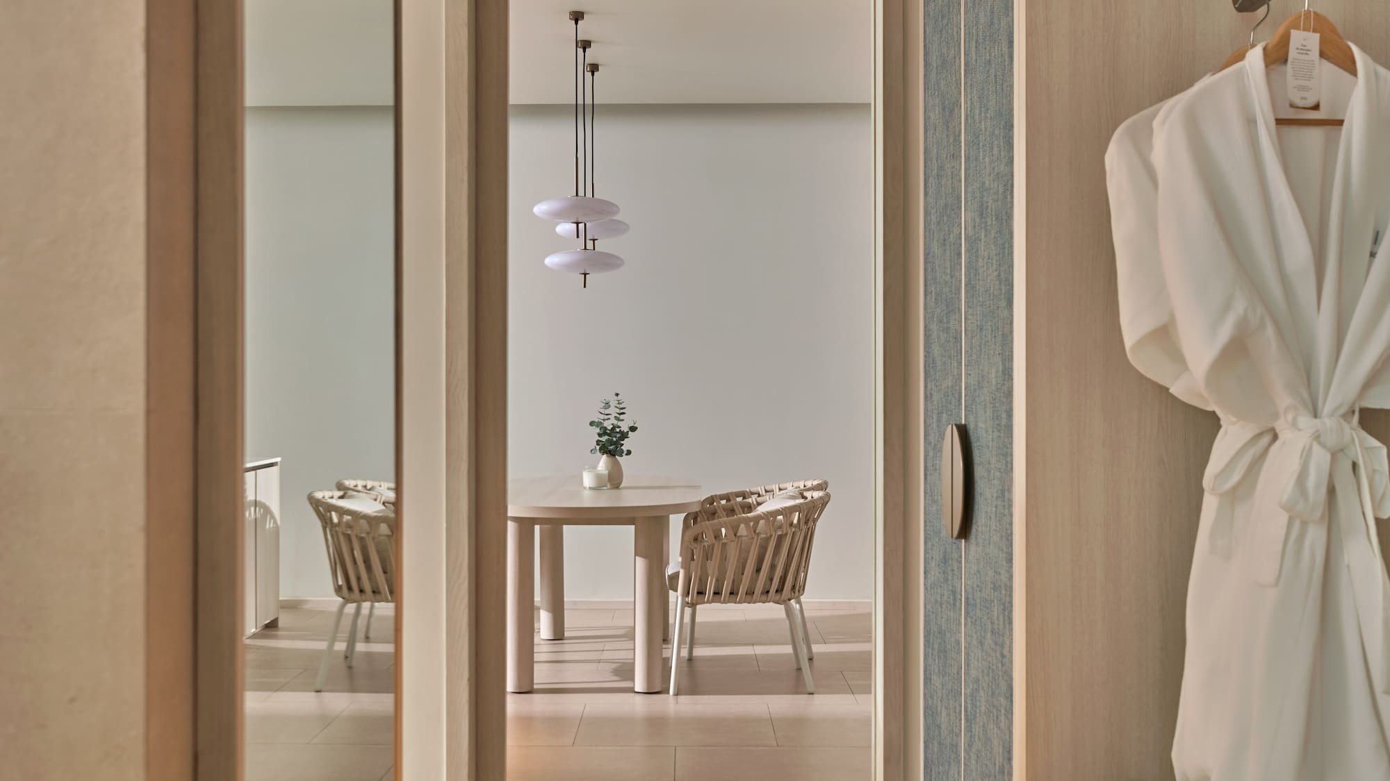 Modern hotel suite: dining area with wicker chairs and hanging robes.