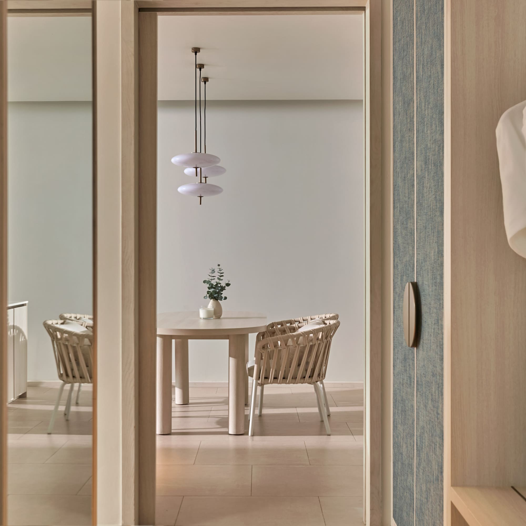 Modern hotel suite: dining area with wicker chairs and hanging robes.