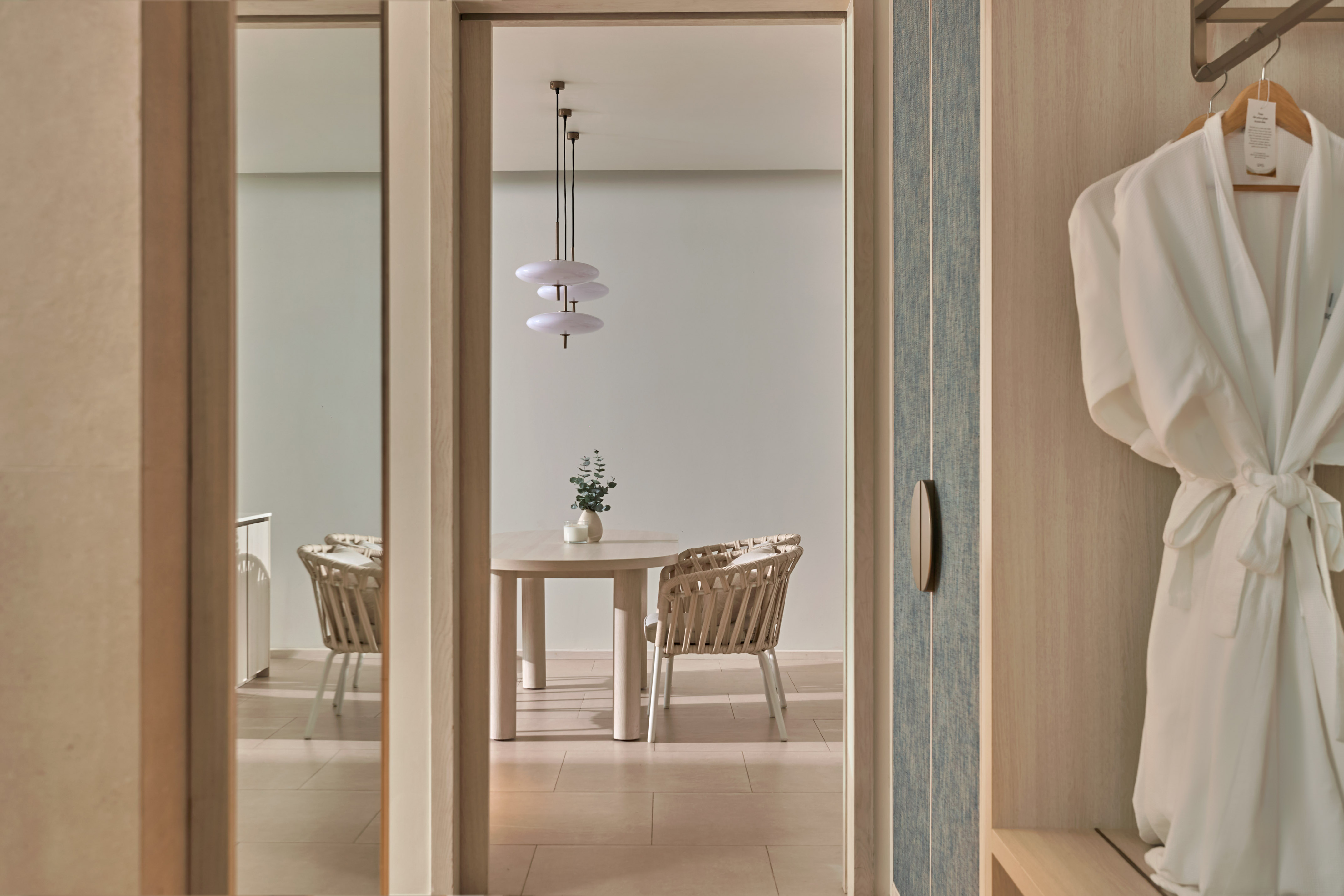 Modern hotel suite: dining area with wicker chairs and hanging robes.
